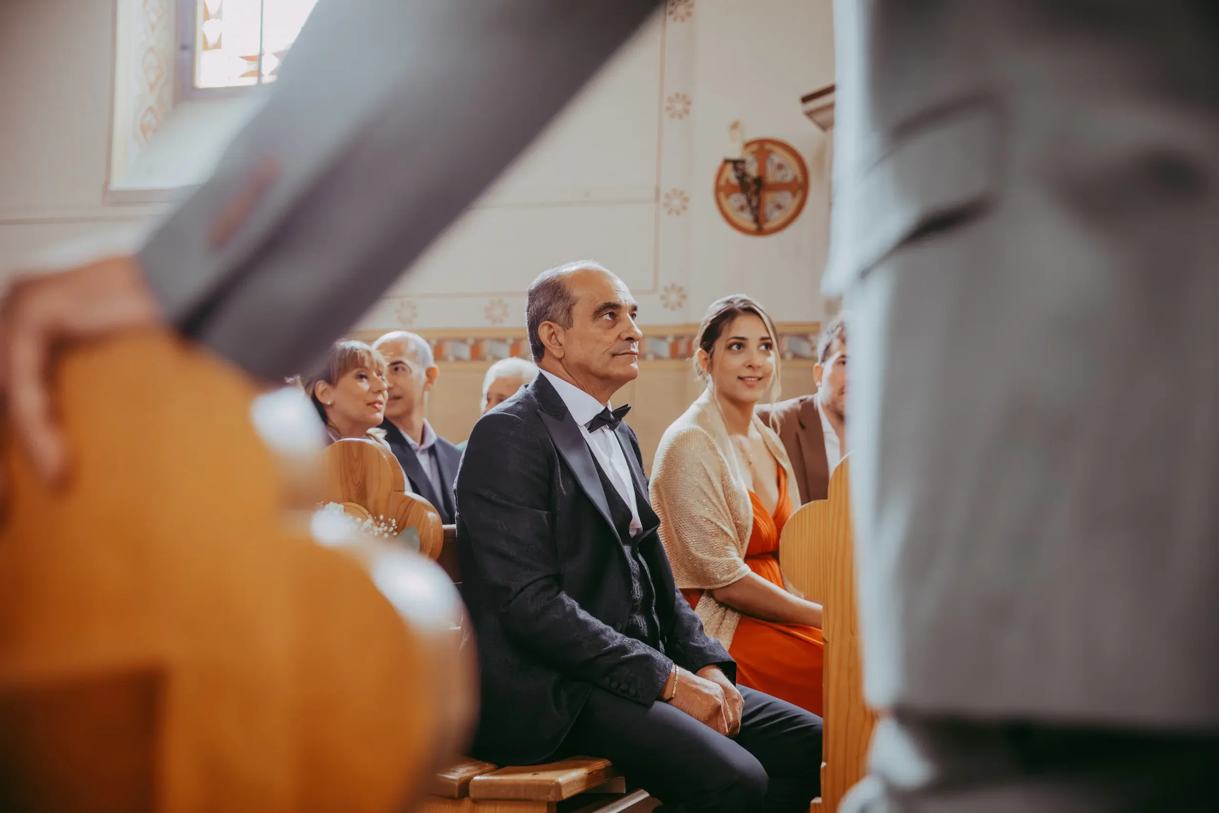 Menschen sitzen in einer Kirche während einer Zeremonie oder Veranstaltung, im Hintergrund eine Wand mit religiösen Symbolen.