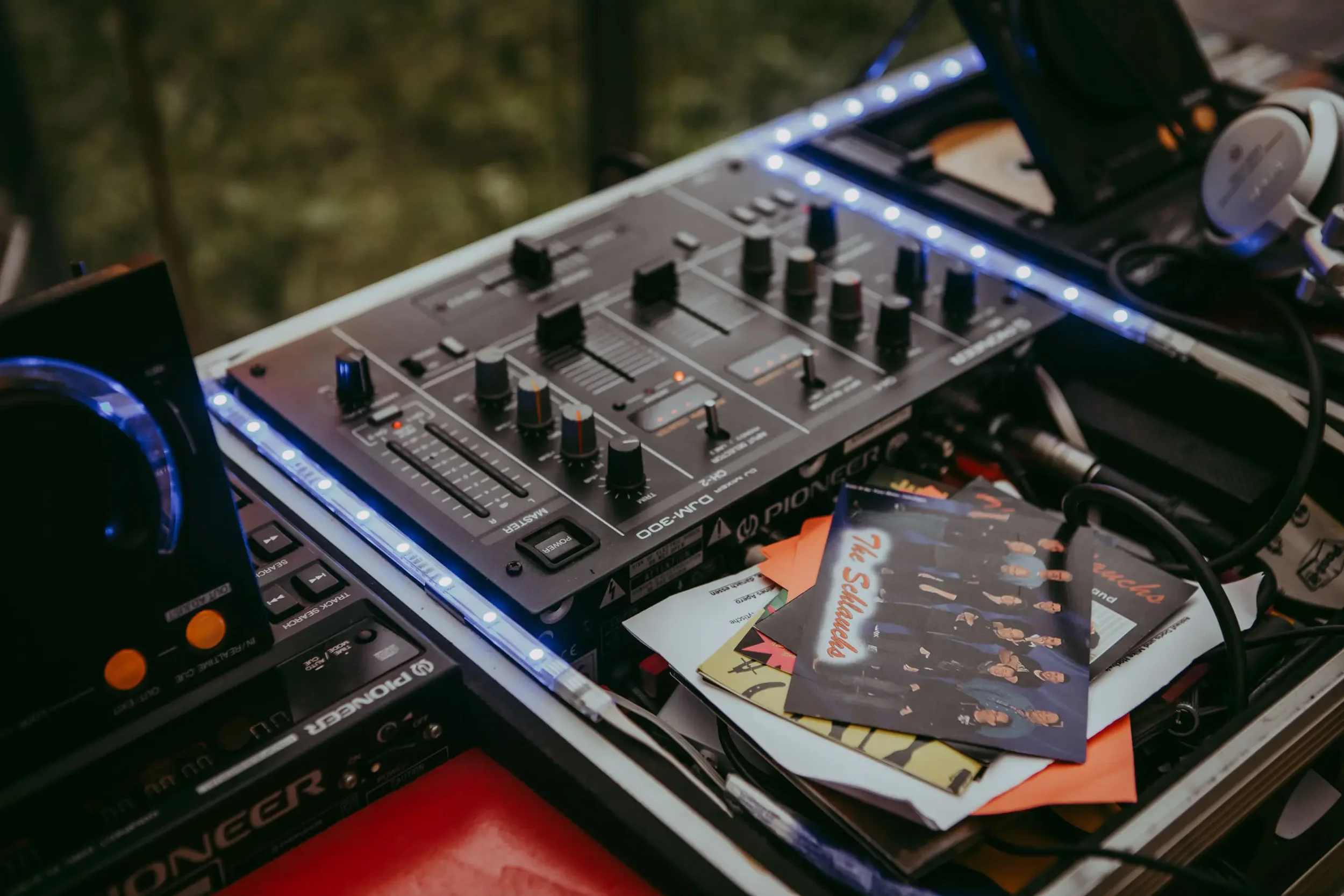 DJ-Controller und Plattenspieler mit Musikmagazinen und CDs auf einem Tisch, Beleuchtung mit blauen LEDs, unscharfer Hintergrund.