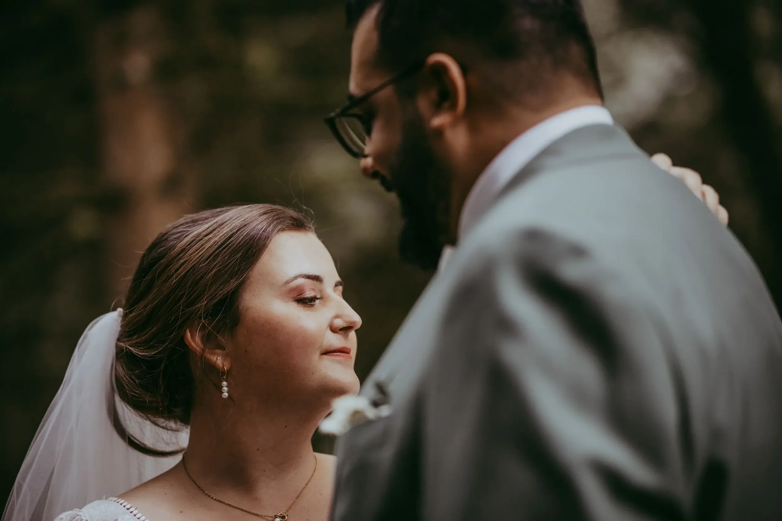 Ein Brautpaar bei einer emotionalen Hochzeit, die Frau mit geschlossenen Augen und einem Lächeln, der Mann beugt sich über sie, um sie zu küssen, im Hintergrund eine Naturkulisse.