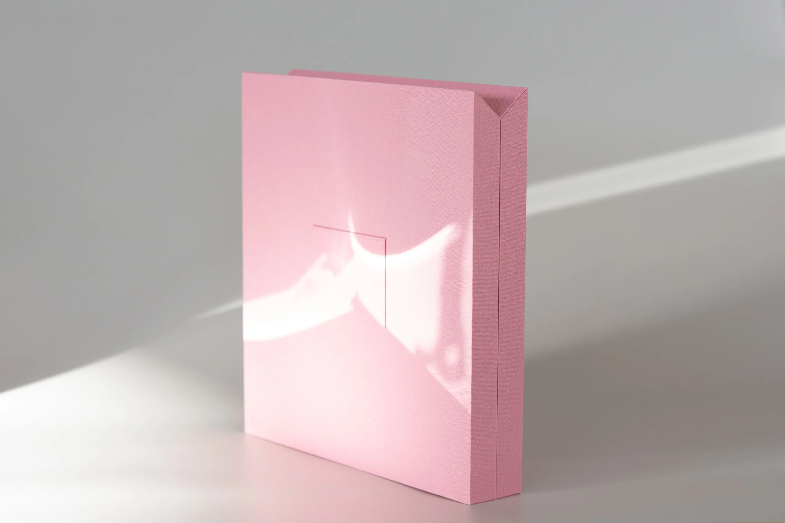 Pinkes, rechteckiges Kunstwerk mit einer Aussparung in der Mitte, das an der Seite steht und Schatten an die Wand wirft.