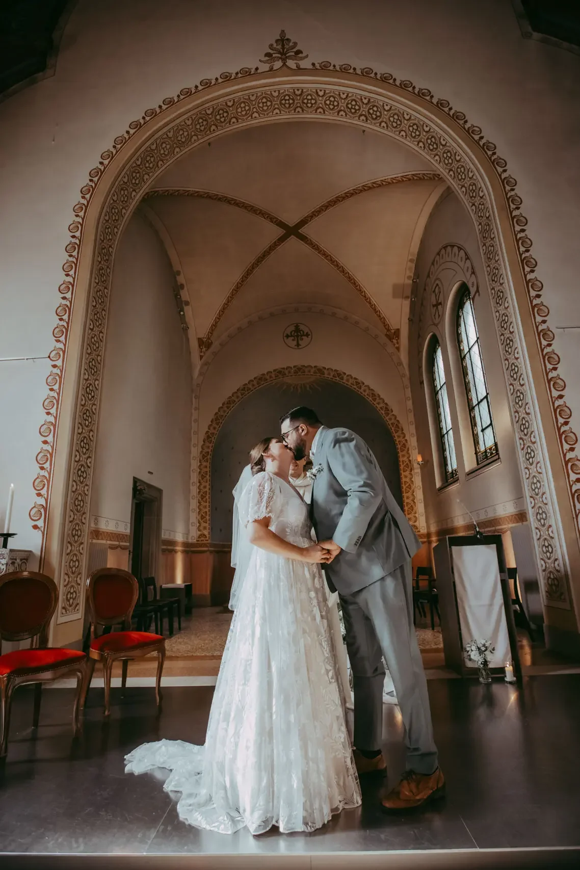 Ein Hochzeitsbild mit einem Brautpaar, das sich im Inneren einer Kirche küsst, umgeben von gotischer Architektur und Buntglasfenstern.