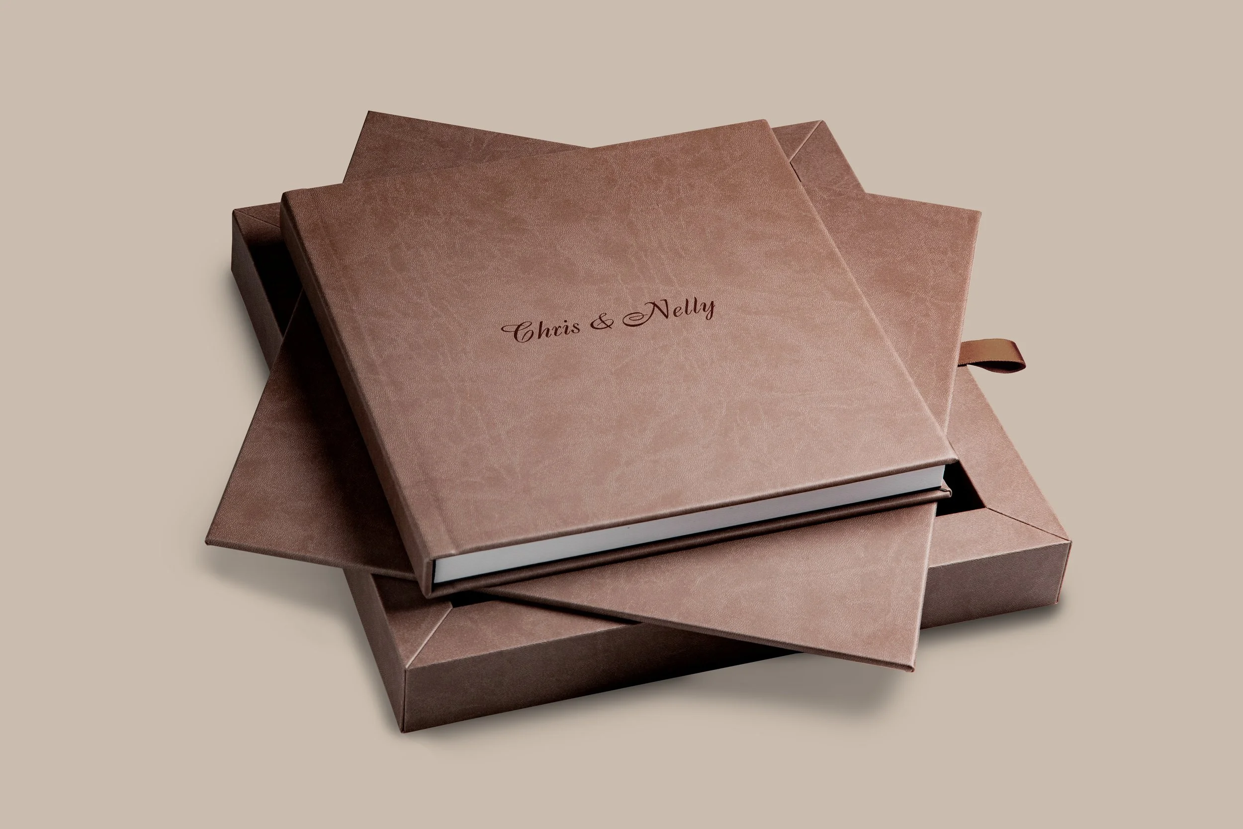 Zwei elegante Geschenkboxen in Bronze- und Taupe-Farben, mit goldener Schrift "Chris & Nelly" auf dem Deckel, auf cremefarbenem Hintergrund.