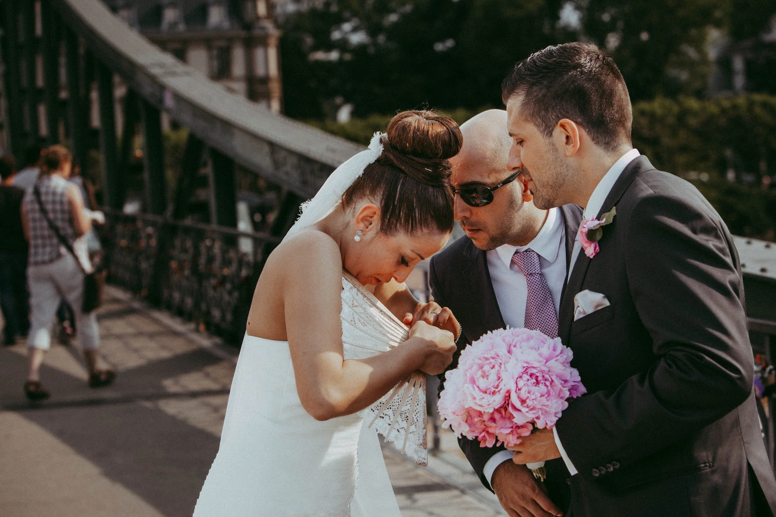 Braut und Bräutigam, die sich auf einer Brücke vor einer Gruppe von Leuten küssen, während die Braut ein Bouquet hält.