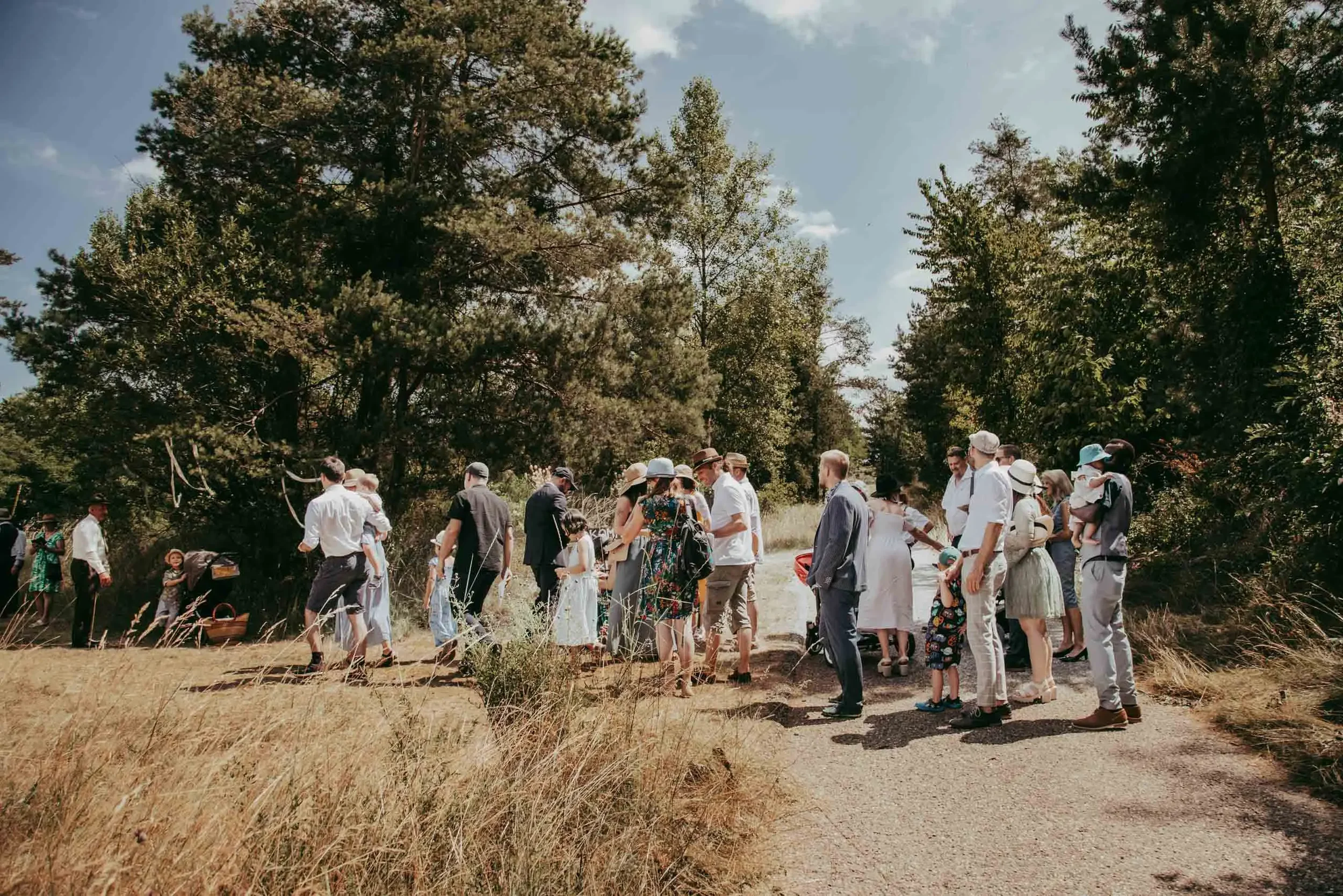 Gruppe von Menschen im Freien, die auf einem Weg stehen, umgeben von Bäumen, bei schönem Wetter.