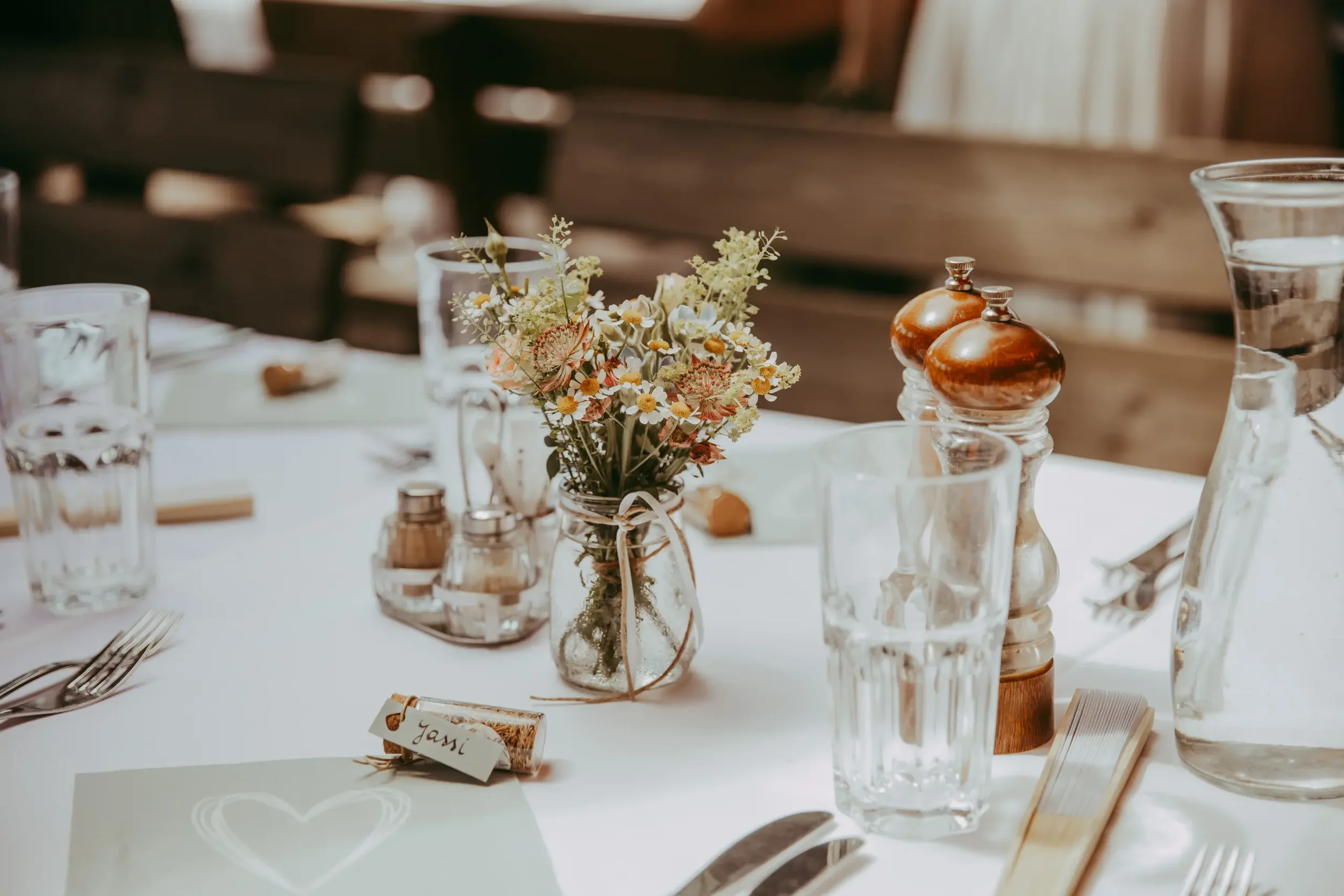 Blumenstrauß auf einem Tisch mit Gläsern und Salz- und Pfefferstreuern bei einer festlichen Veranstaltung.
