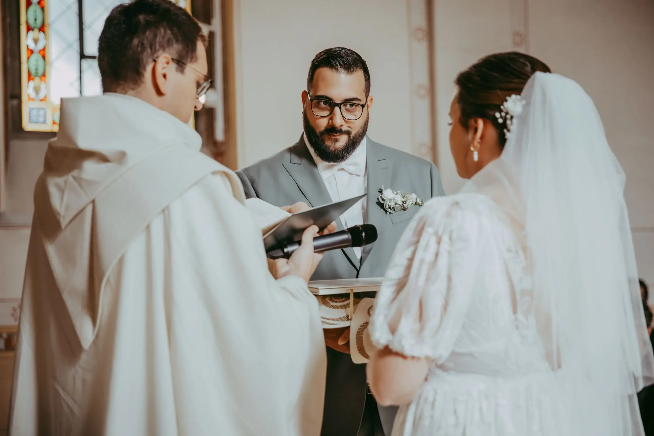 Ein Mann in einem Anzug bei einer Hochzeitszeremonie, der vor einem Paar steht, das in Brautkleid und Anzug gekleidet ist, während ein weiteres Paar eine Zeremonie durchführt.