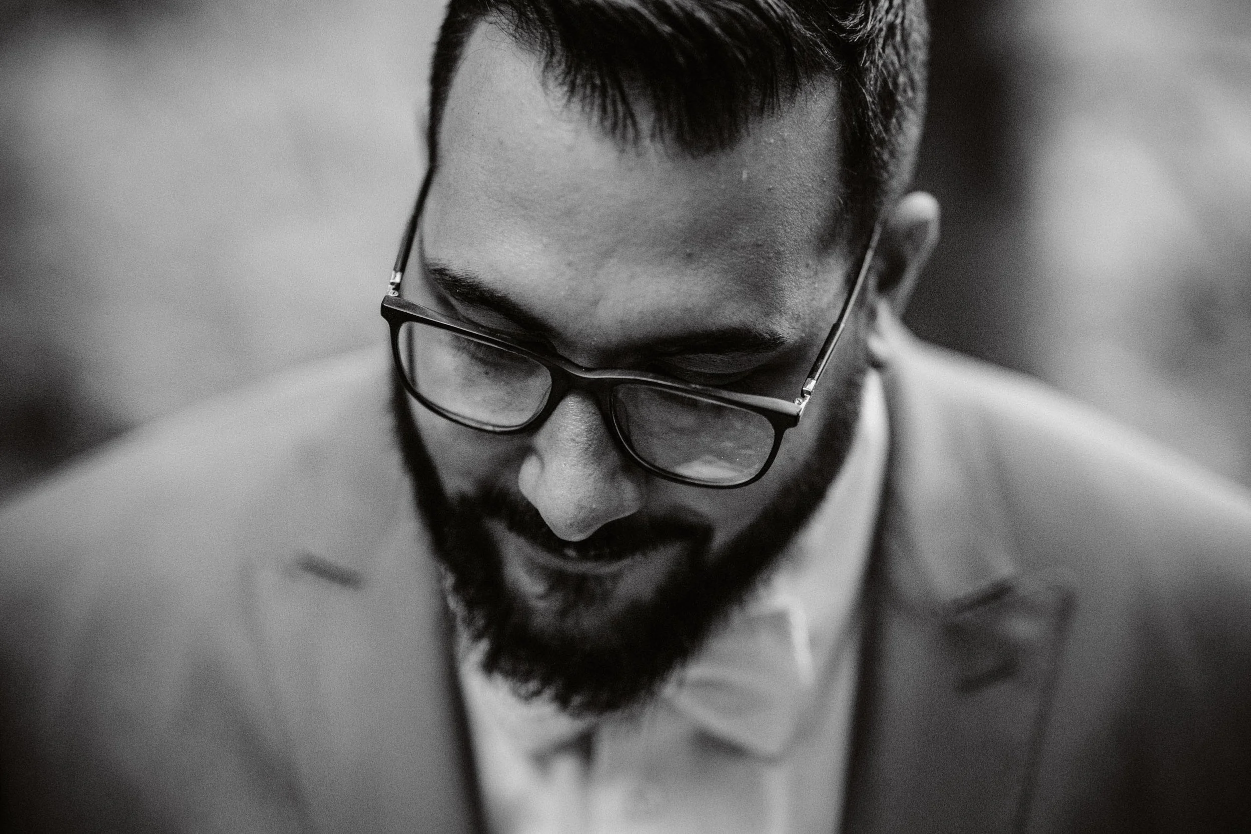 Schwarze und weiße Nahaufnahme eines Mannes, der eine Brille trägt und nach unten schaut.
