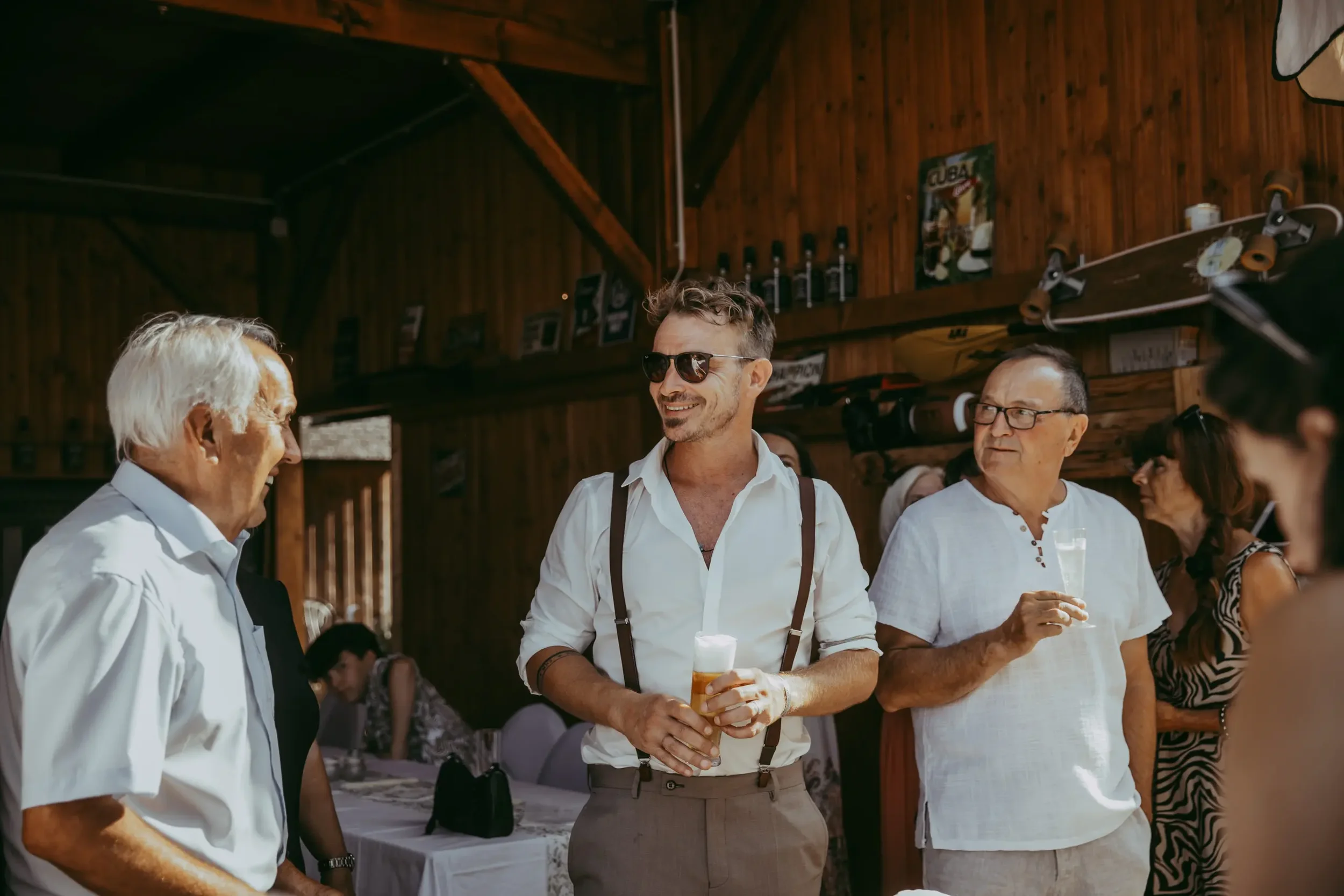 Mehrere Menschen beim geselligen Beisammensein in einem Holzhaus, einige halten Getränke in der Hand, die Stimmung ist fröhlich.