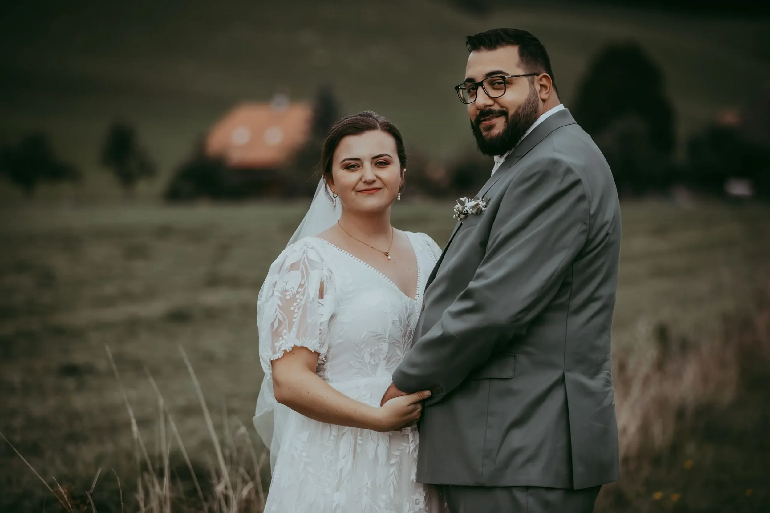 Ein Brautpaar bei einer Hochzeit im Freien, ein Mann in einem grauen Anzug und eine Frau in einem weißen Hochzeitskleid, die sich halten.
