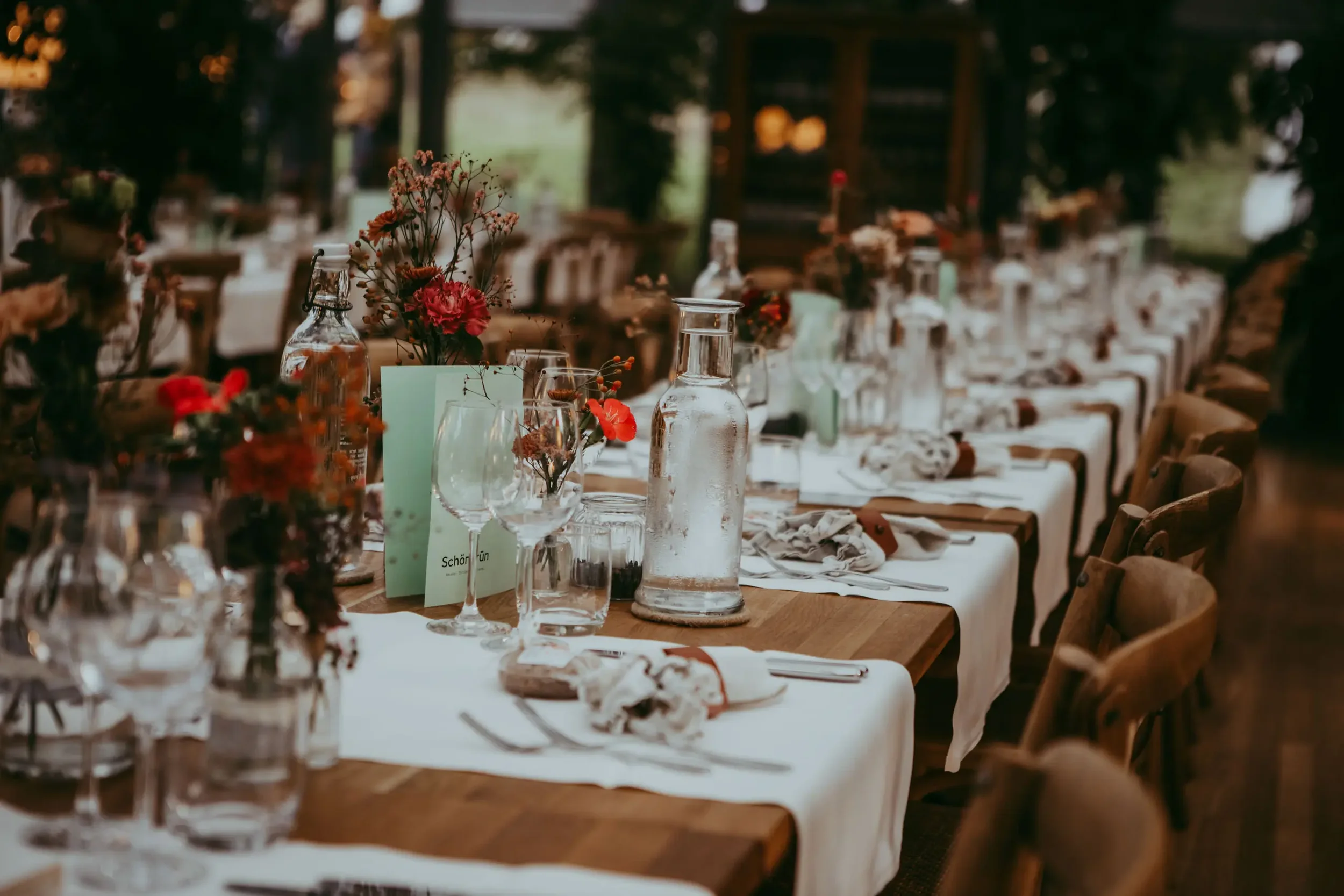 Ein festlich gedeckter Tisch mit Gläsern, Vasen und Blumen in einem rustikalen Raum, vermutlich für eine Feier oder ein Event.