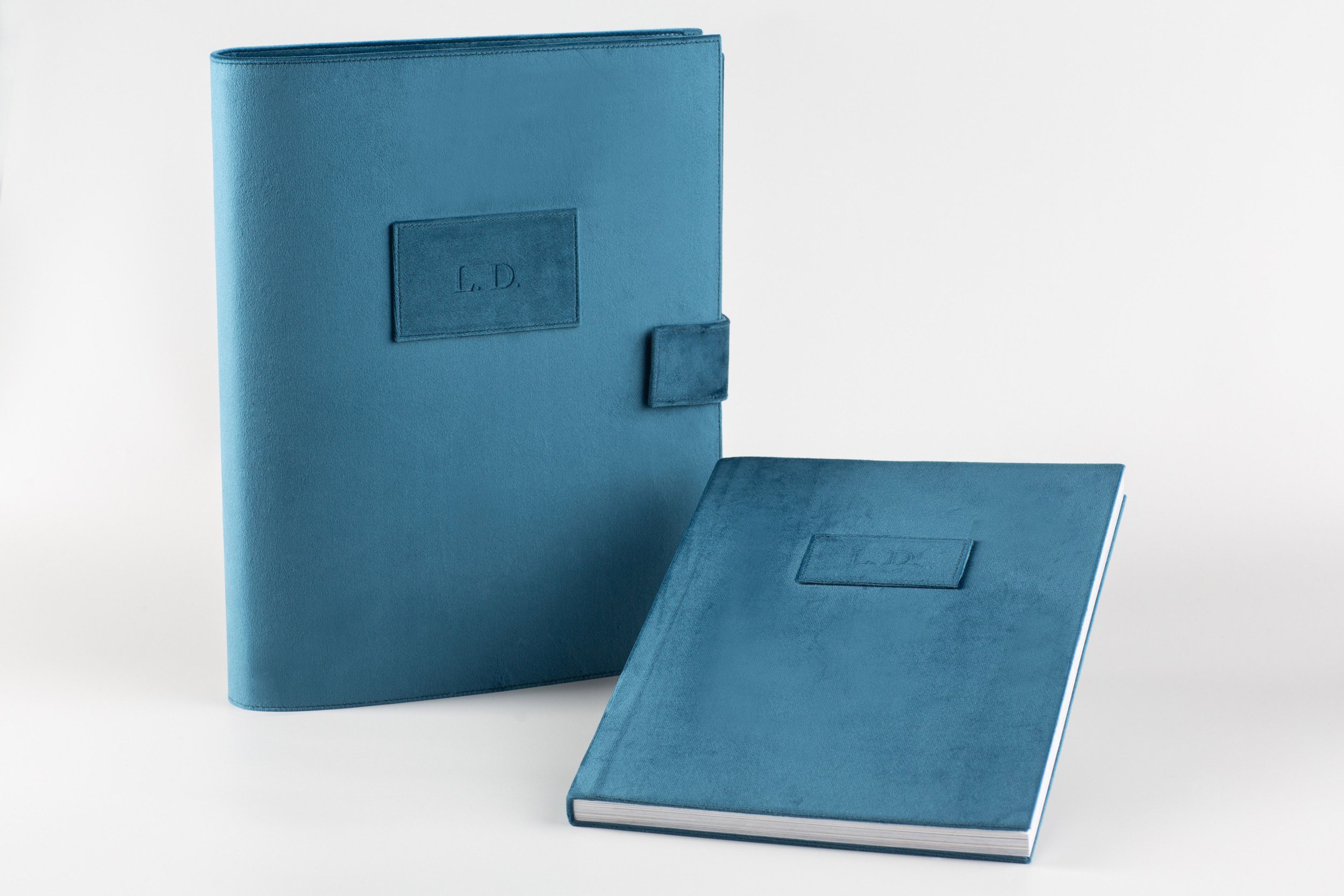Drei blaue Buchhüllen, eine steht aufrecht, eine liegt flach und eine ist in der Mitte leicht geöffnet.