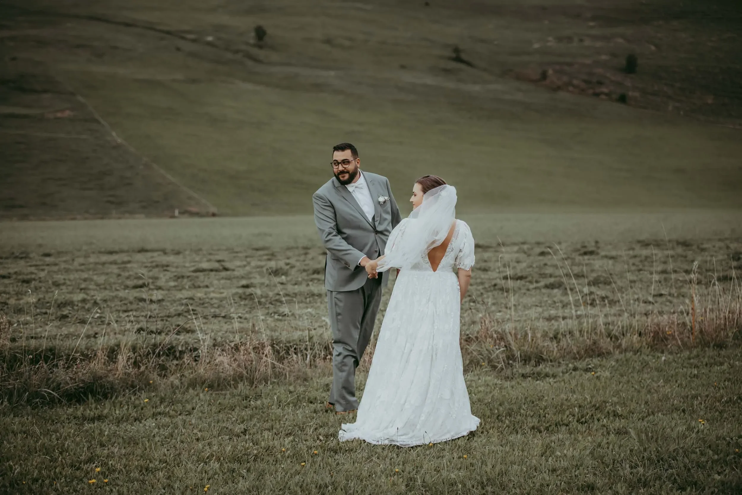 Ein frisch verheiratetes Paar bei einer Hochzeit im Freien auf einer Wiese, mit einem Berg im Hintergrund.