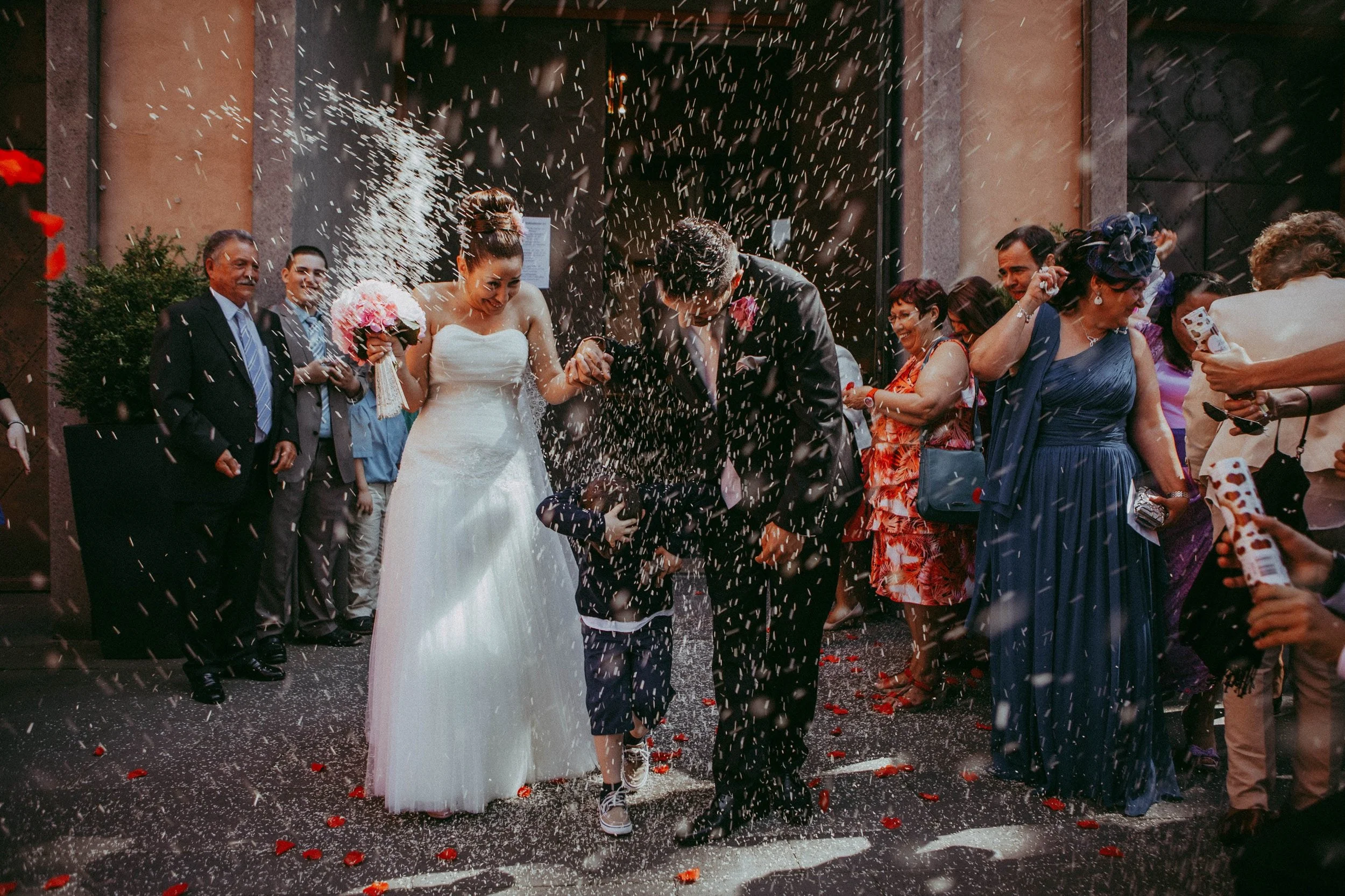 Hochzeitspaar beim Durchqueren eines Feuerwerks oder Konfetti, umgeben von Gästen im Freien.