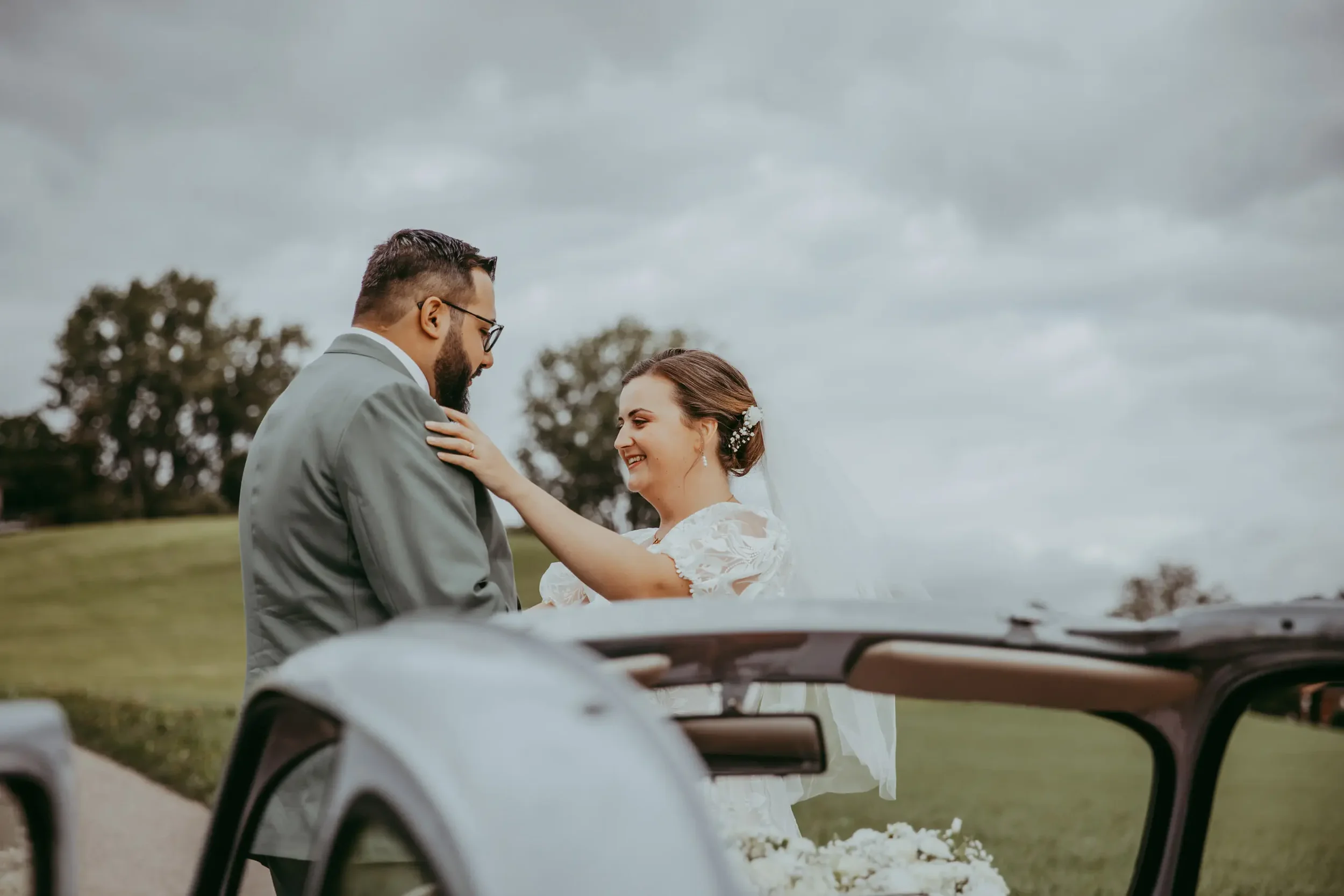 Ein Brautpaar bei einer Hochzeit, die auf einem Feld im Freien stattfindet, umgeben von Bäumen bei bewölktem Himmel.