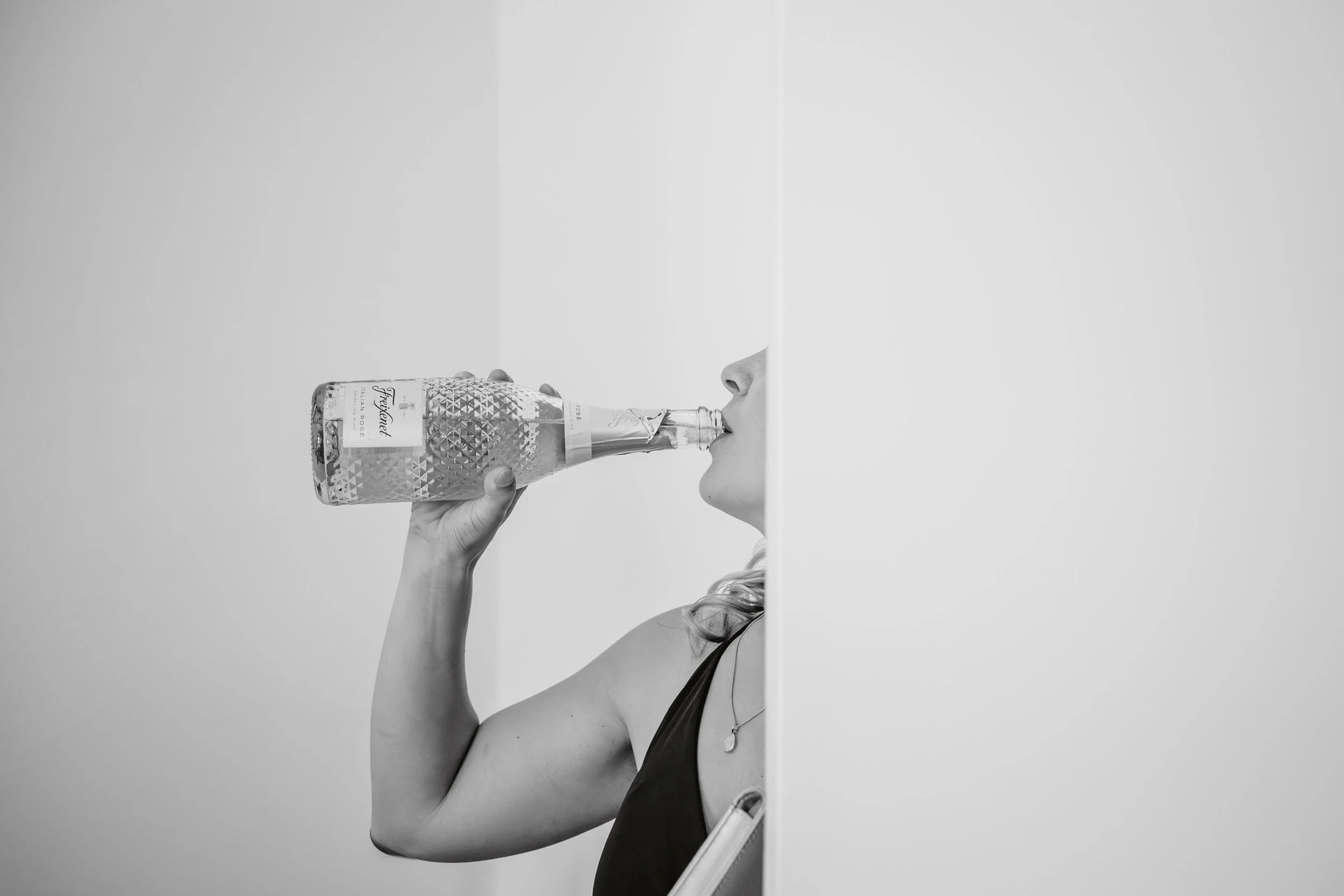 Schwarz-weiß-Bild einer Frau, die ein Glas Wasser trinkt, halb hinter einer weißen Wand sichtbar.