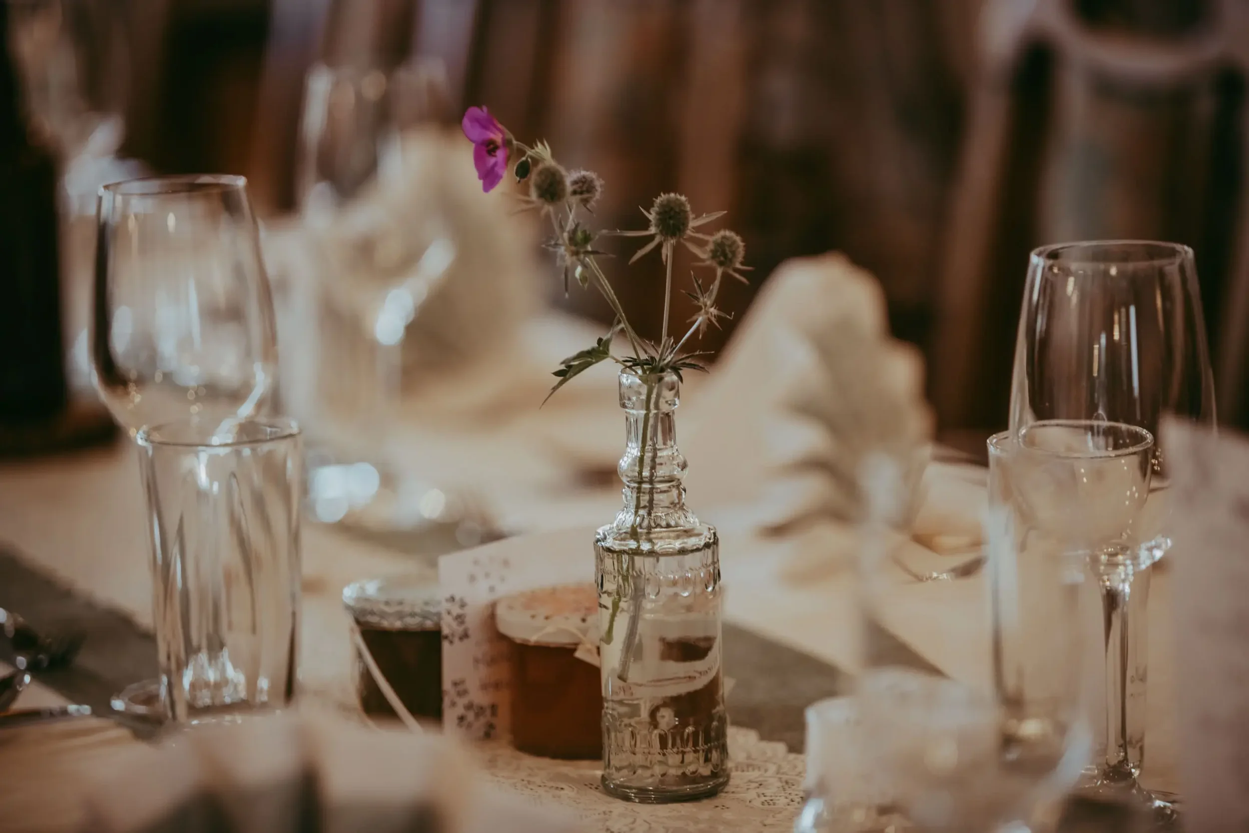Blumen in kleinen Gläsern auf einem Tisch, umgeben von leeren Gläsern, bei einer festlichen Mahlzeit