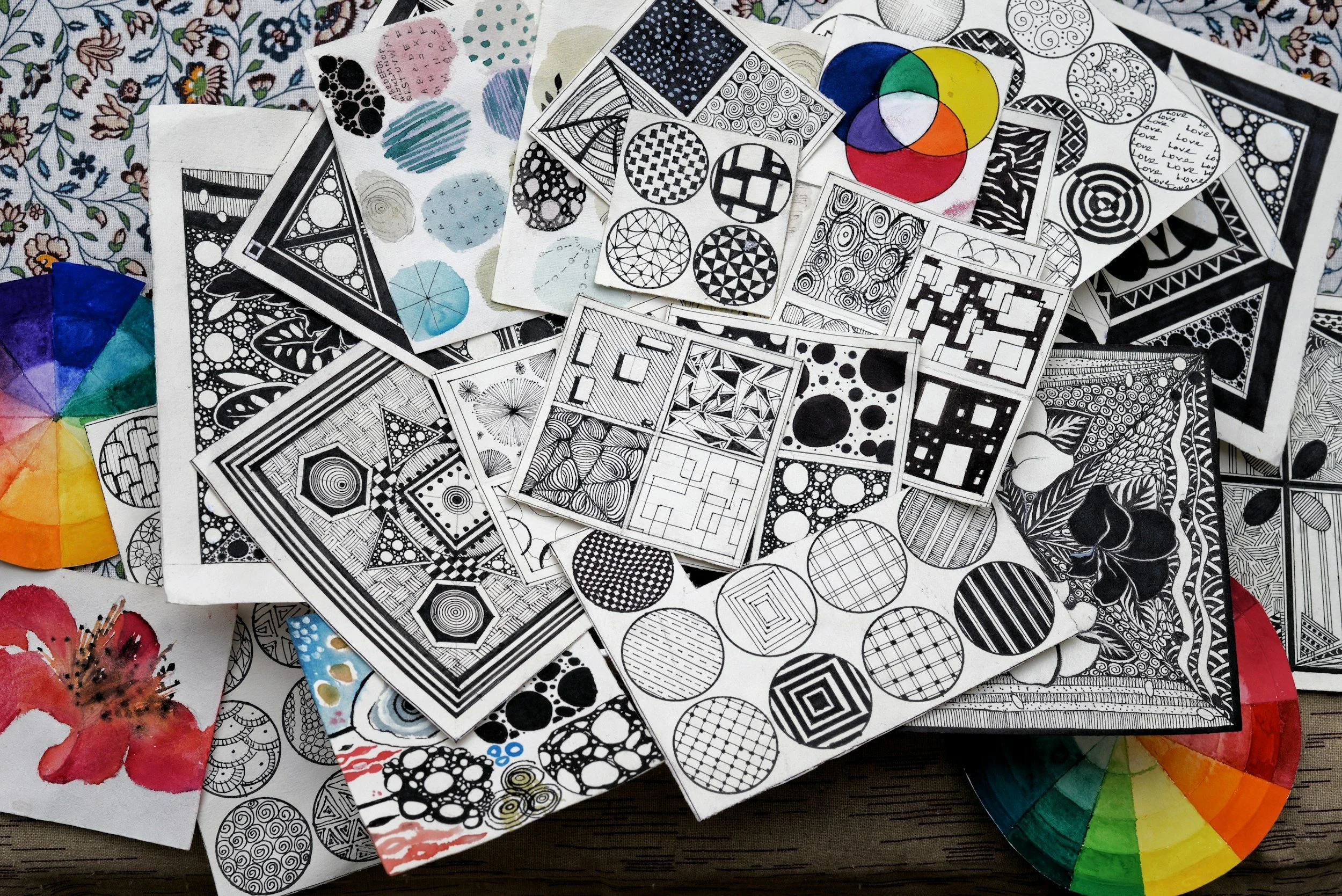 A collection of small black and white Zentangle art sketches on paper, complemented by a color wheel palette and watercolor swatches.
