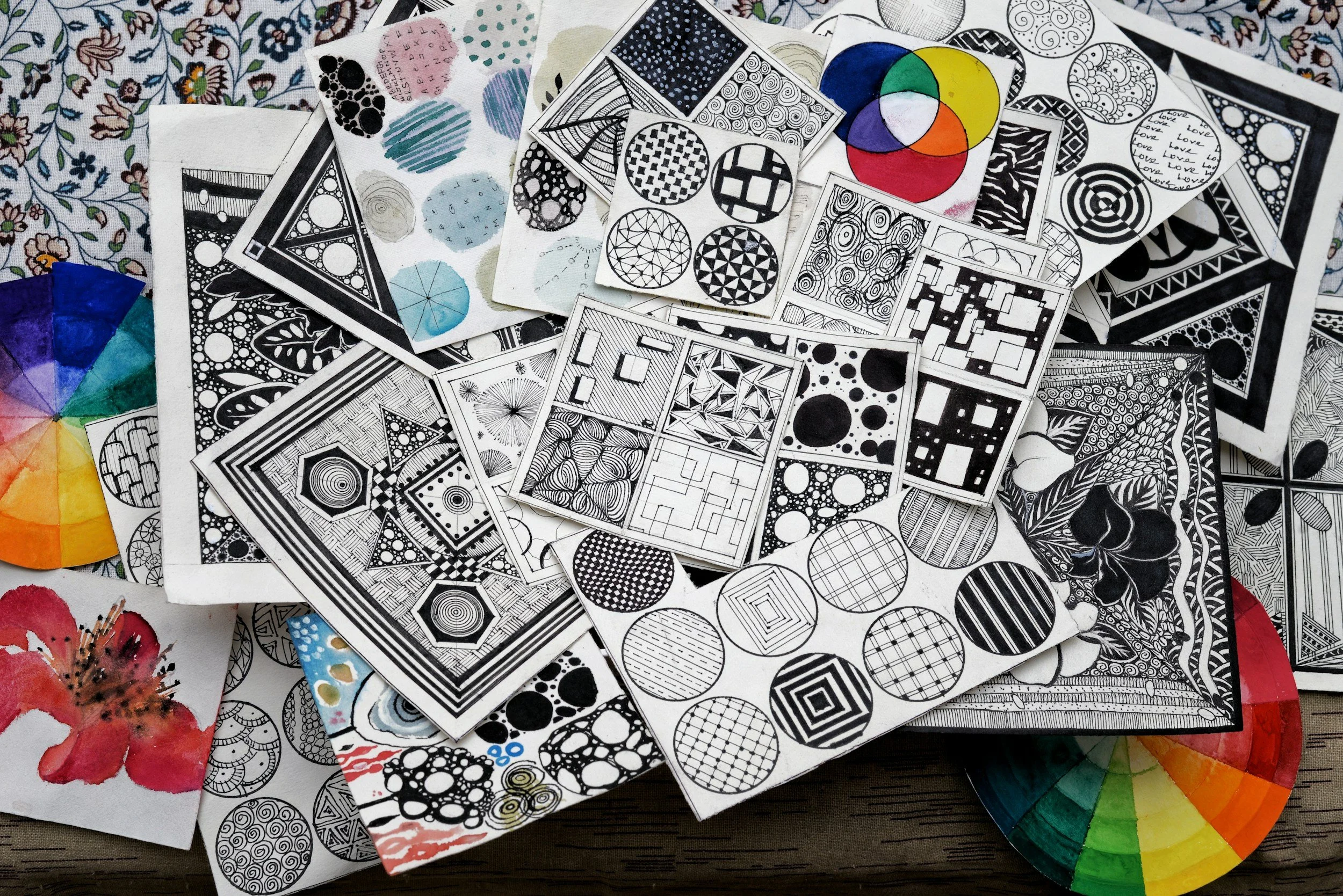 A variety of black and white illustrated pattern sheets on a table, with some color swatches and floral illustrations around them.
