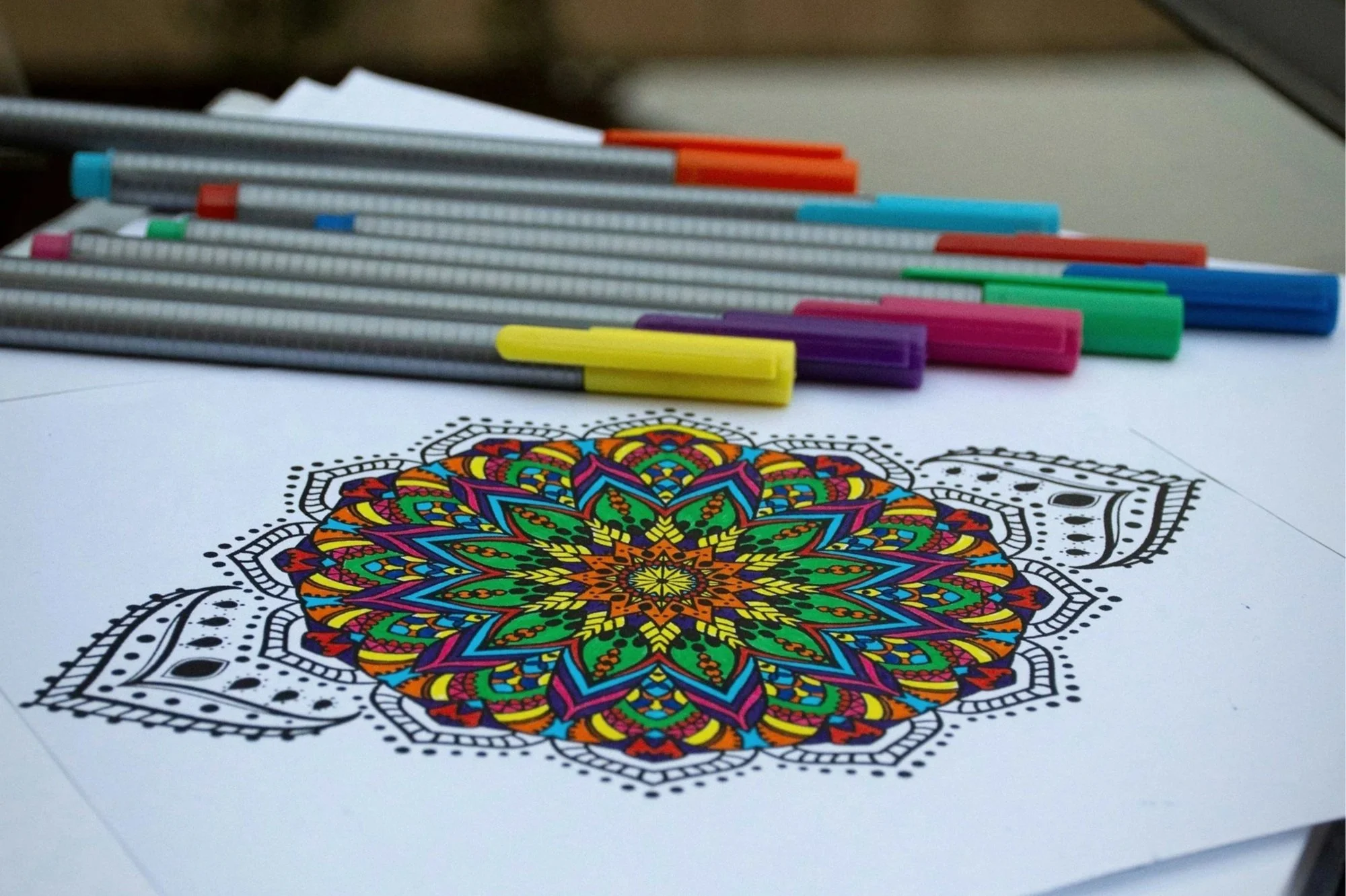 Colorful mandala design on paper with multiple colored markers placed above it.