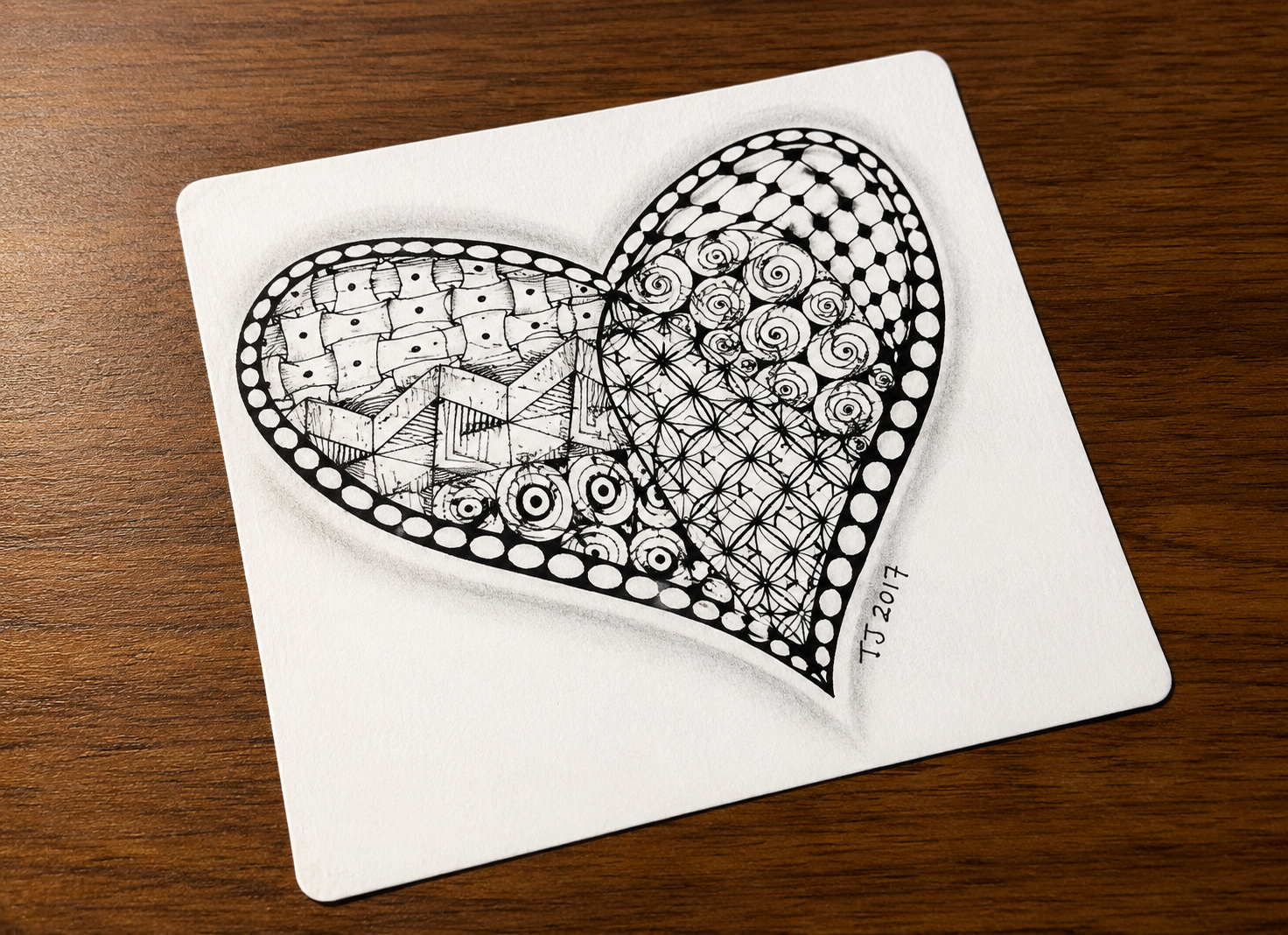 A paper with a heart-shaped doodle featuring various geometric patterns and circular designs, signed 'TS 2017' in the bottom right corner.