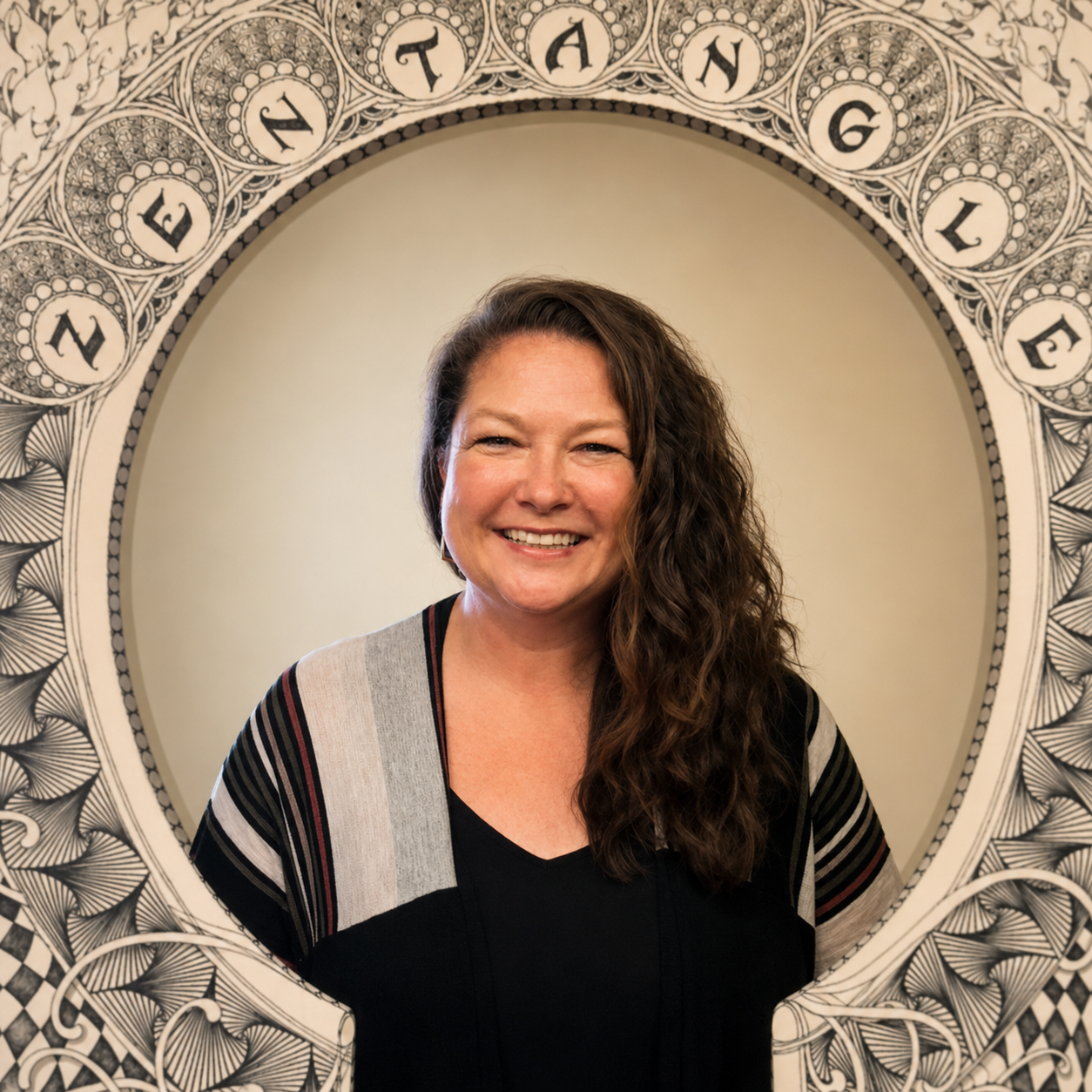 A woman with long, curly brown hair smiling at the camera, standing in front of an ornate circular frame with the word 'Imagine' written at the top.