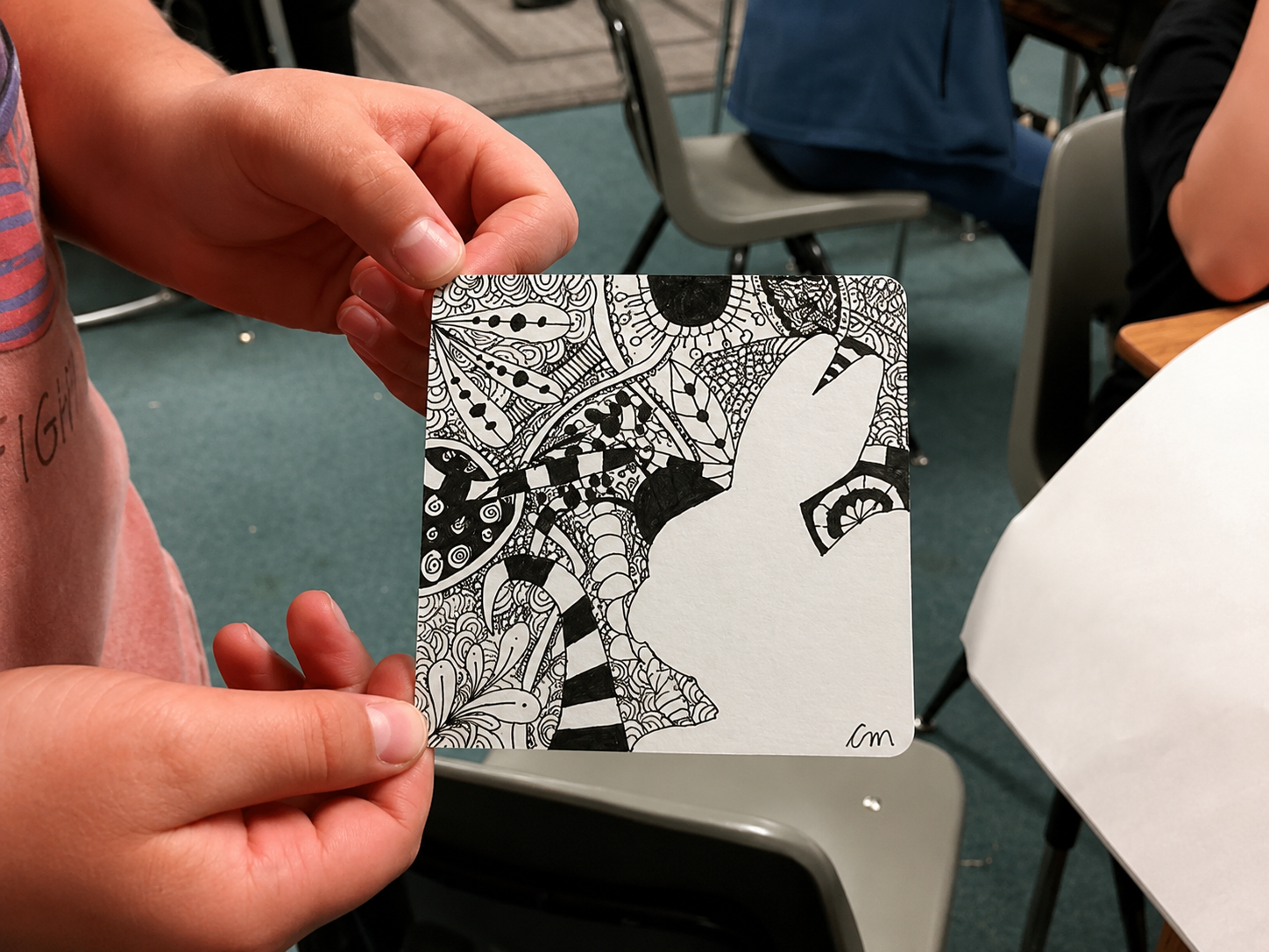 Person holding a black and white abstract illustration featuring a silhouette of a dog's face surrounded by intricate patterns and designs.