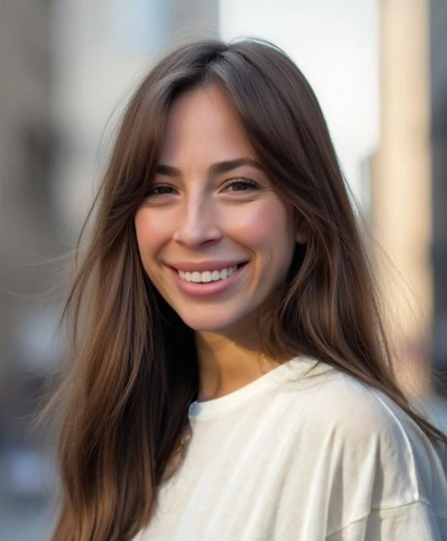 A young woman with long brown hair smiling outdoors on a sunny day.