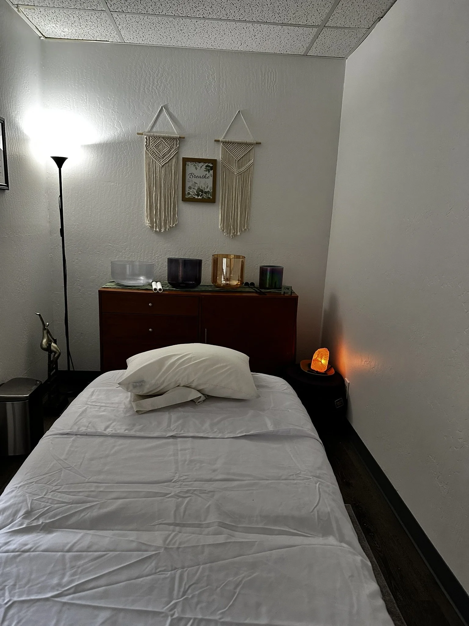 Peaceful sound healing room with a massage table, crystal singing bowls, pillows, and a glowing salt lamp