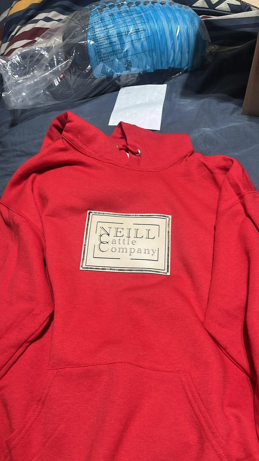 Red hoodie with a white rectangular patch on the front reading 'NELL Cattle Company.'