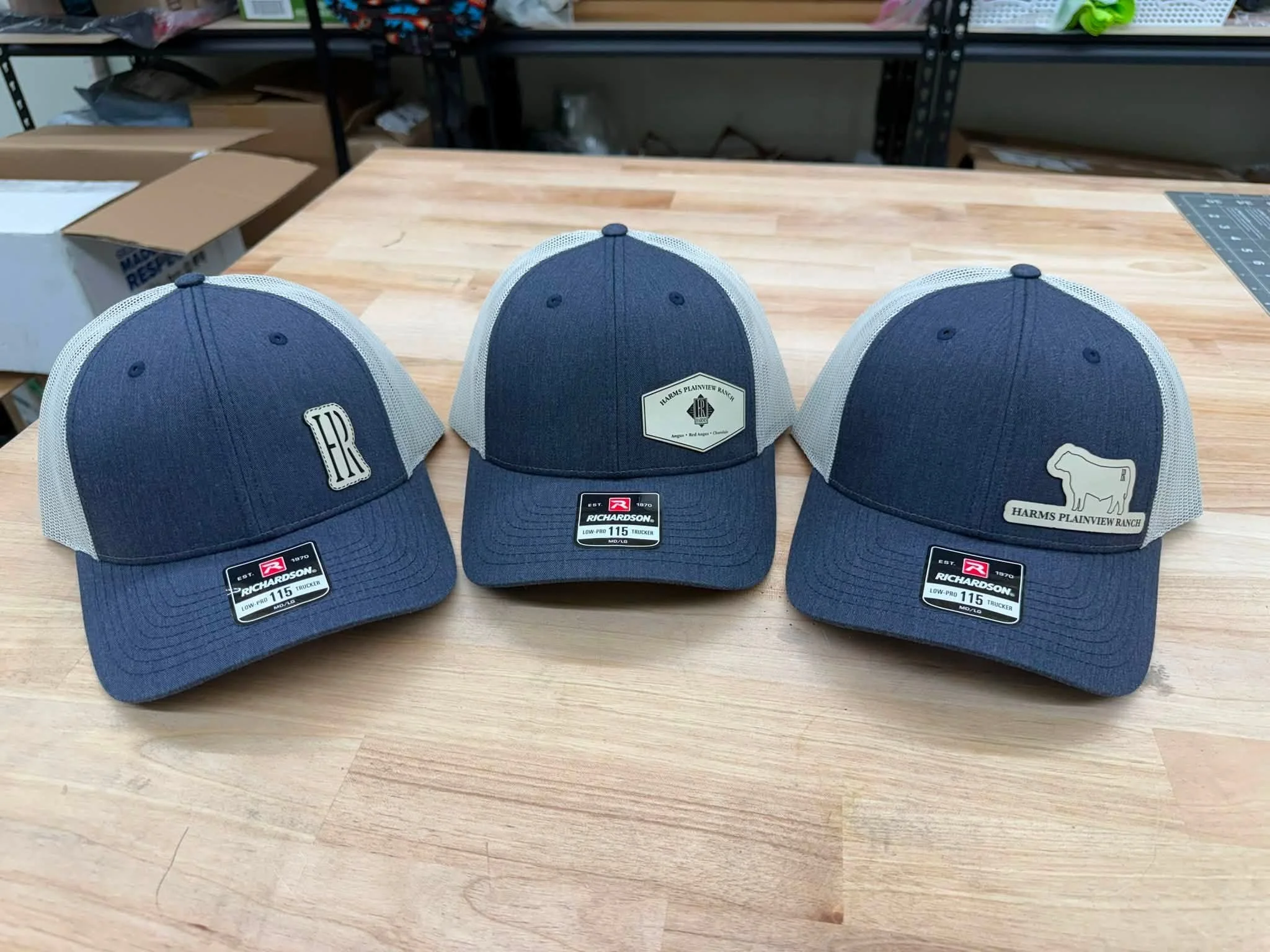 Three blue mesh-backed baseball caps with patches and labels on a wooden table.