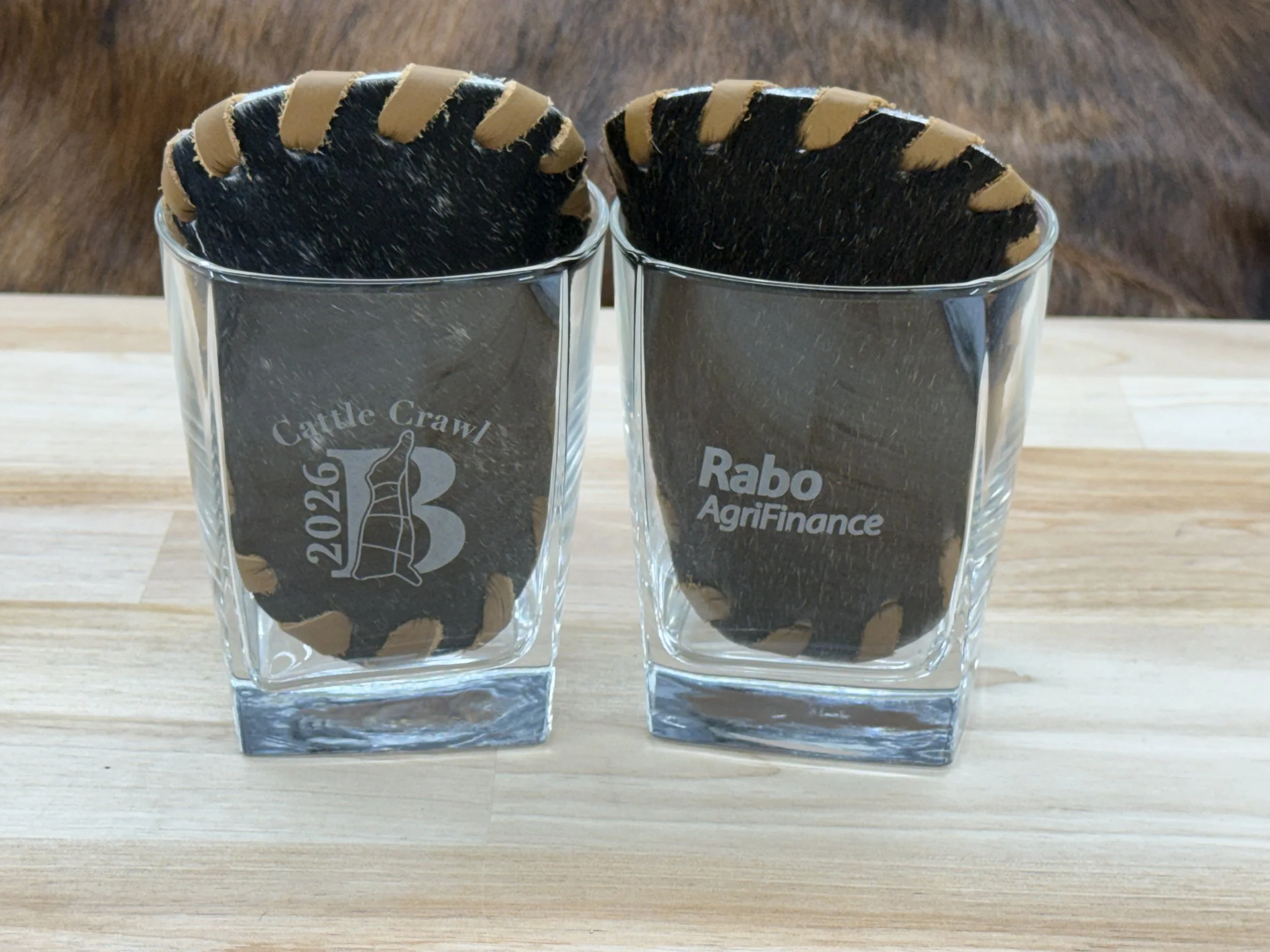 Two glass cups filled with large, round, black coasters with a brown edge, placed on a wooden surface.
