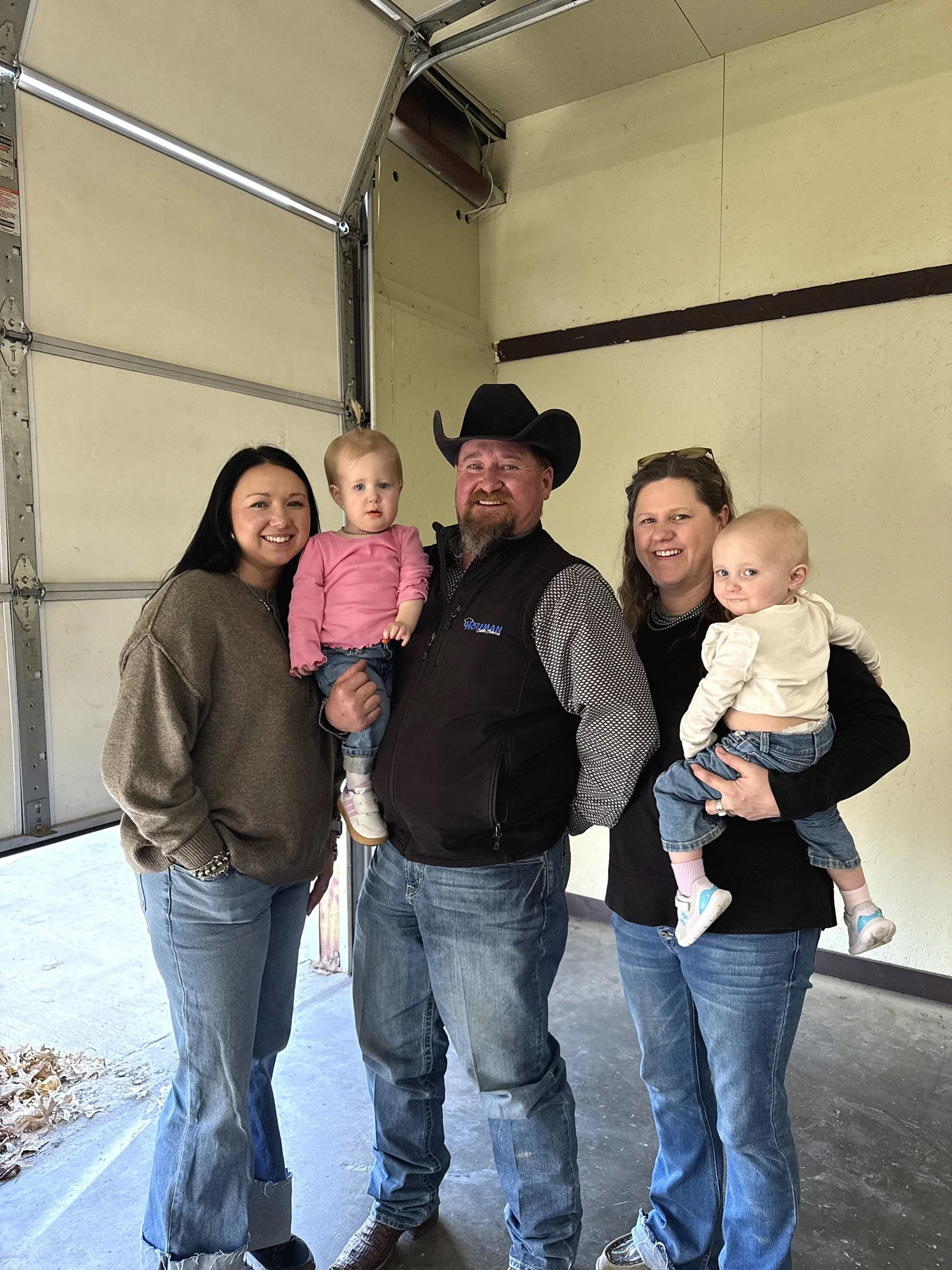 A group of four women, a man, and two young children standing inside a garage, smiling at the camera.