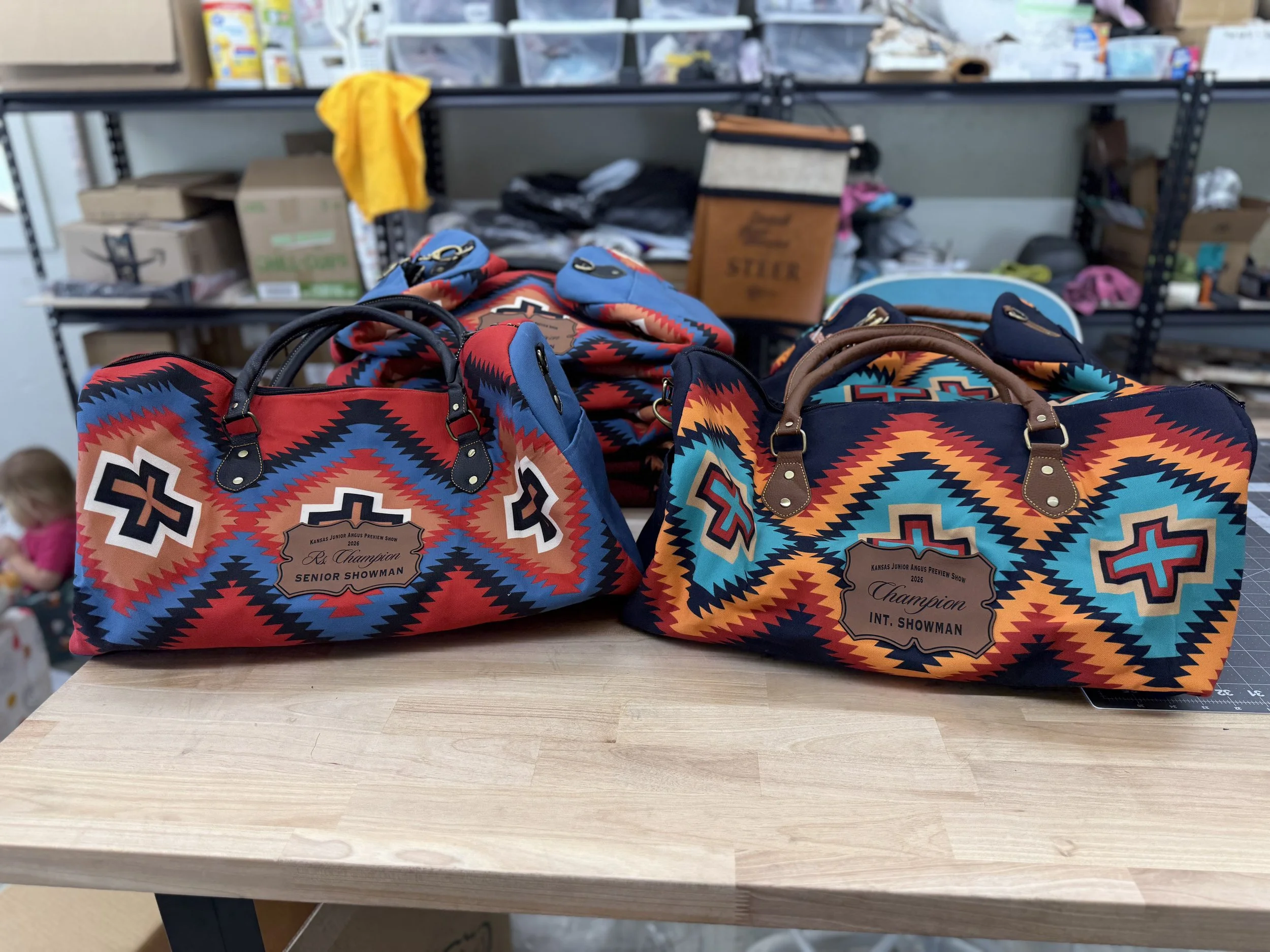 A collection of colorful bags with southwestern patterns placed on a wooden table, with a background of shelves filled with various boxes and items.