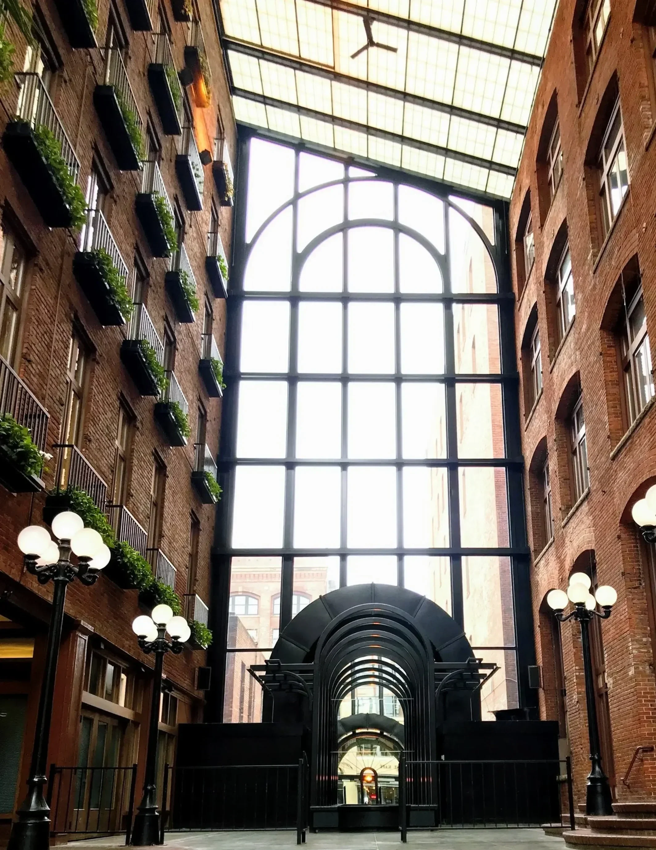 Interior view of a building with brick walls, large arched glass roof, decorative street lamps, and a gated entryway.