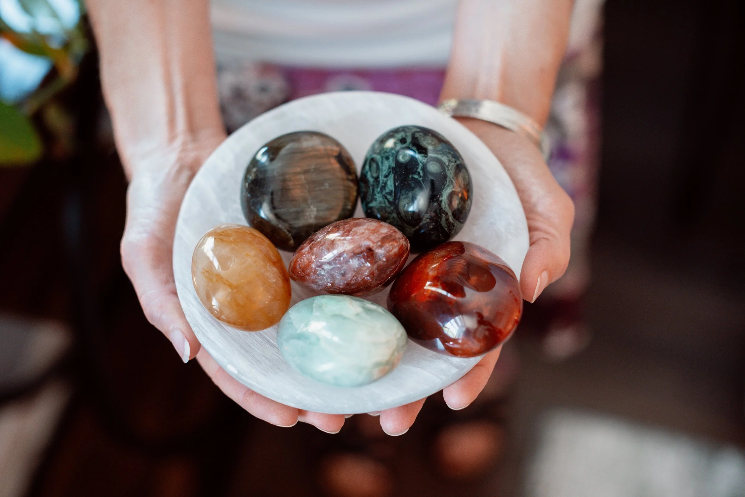 A person holding a white dish with several polished, colorful stones, including black, brown, orange, and green stones.