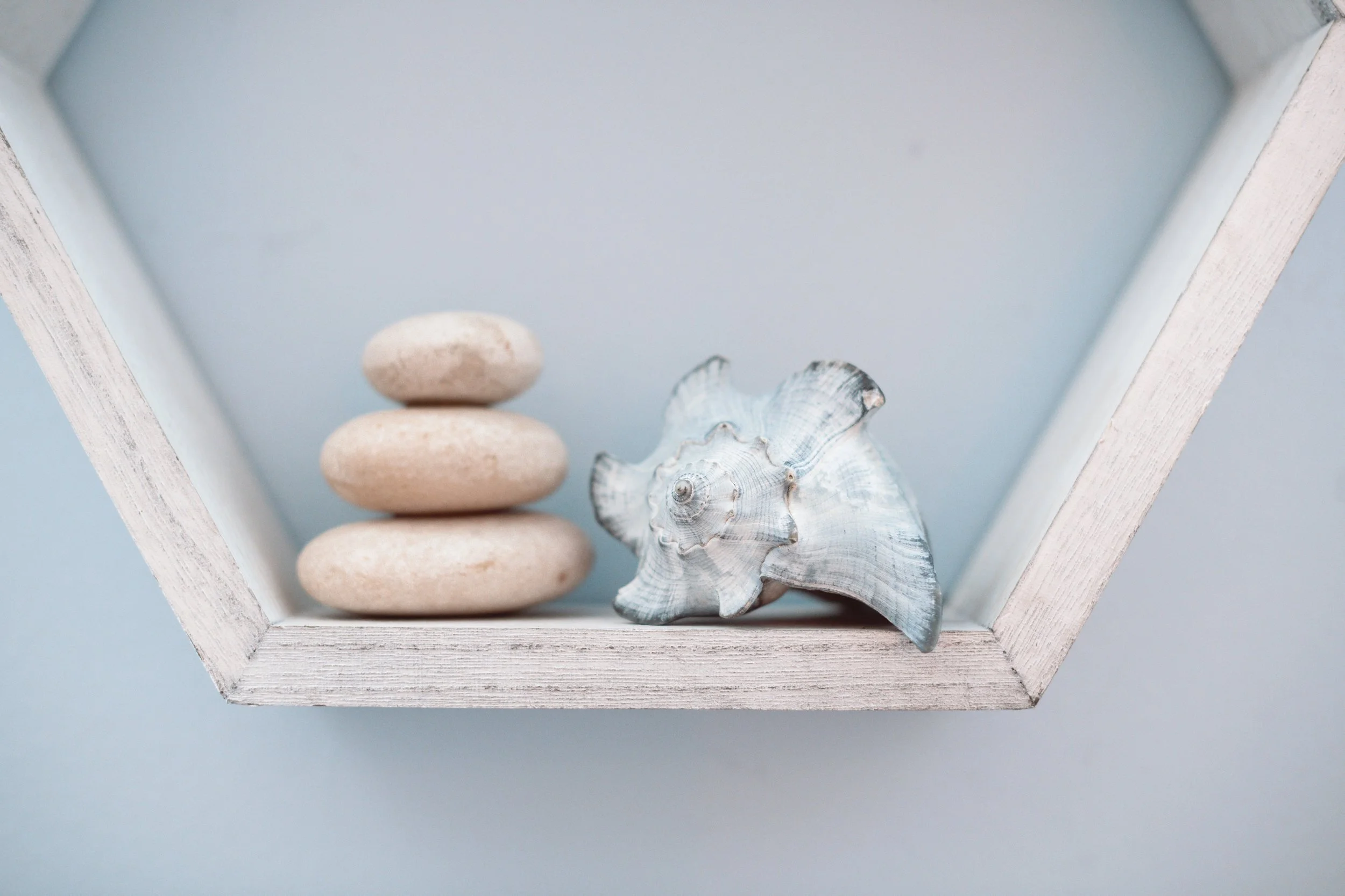 A white wooden box with a light blue interior containing a stack of four smooth, rounded stones, a seashell, and a starfish.