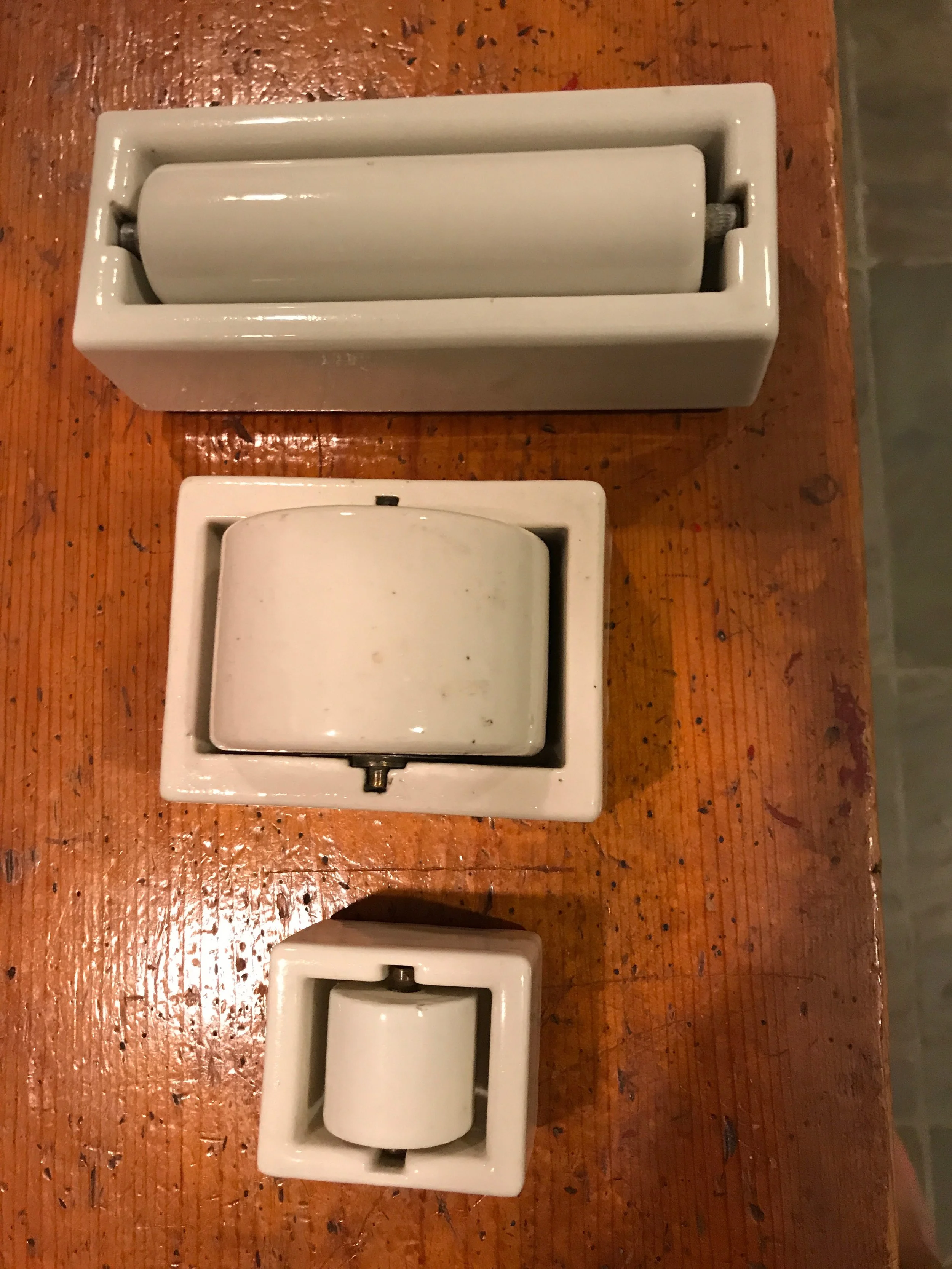 Three white ceramic napkin or soap dish holders in individual plastic packaging, placed on a wooden surface.