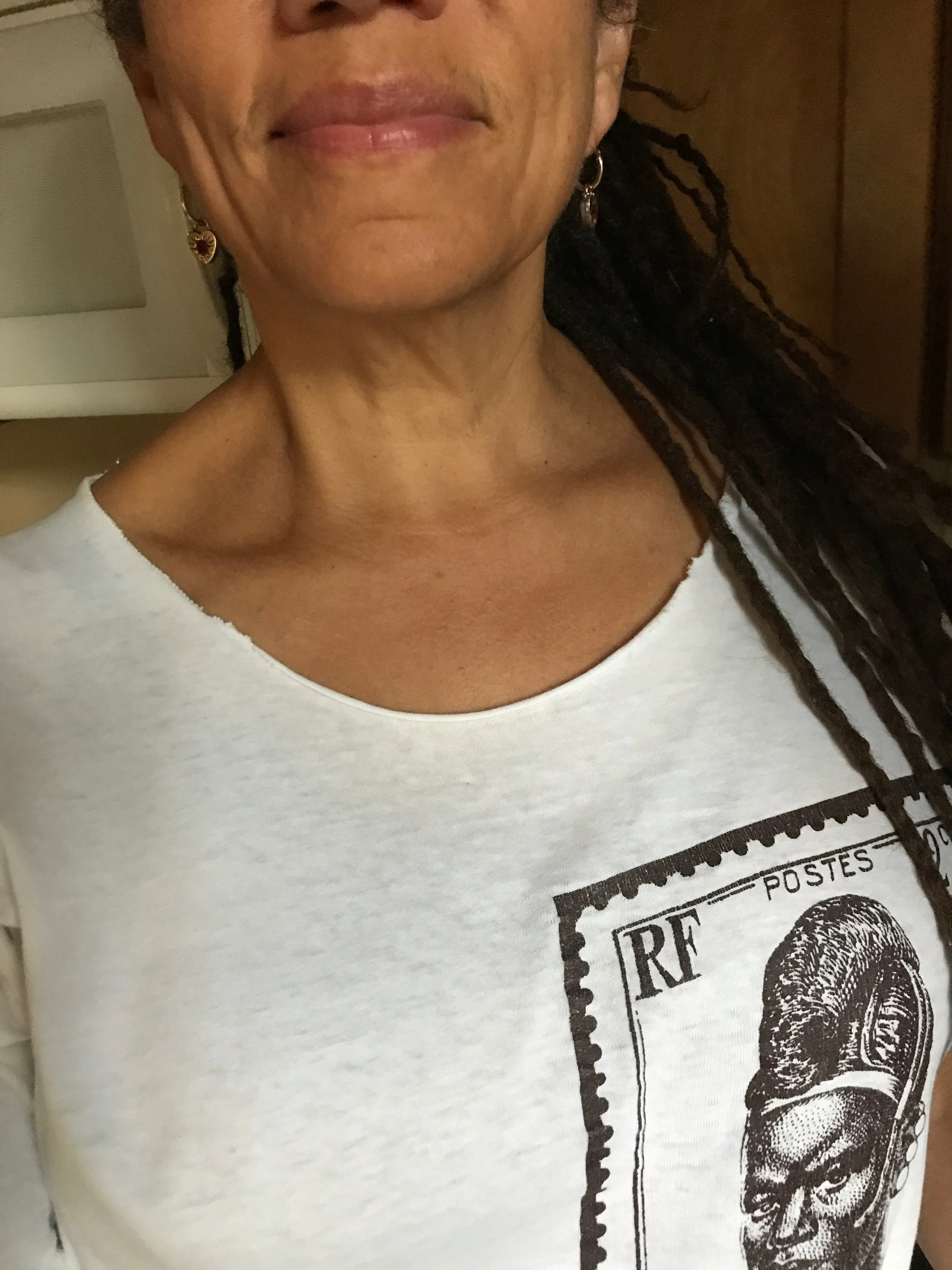 Close-up of a person's face, showing lips and part of a nose, with earrings and a white T-shirt featuring a postage stamp design with a portrait.