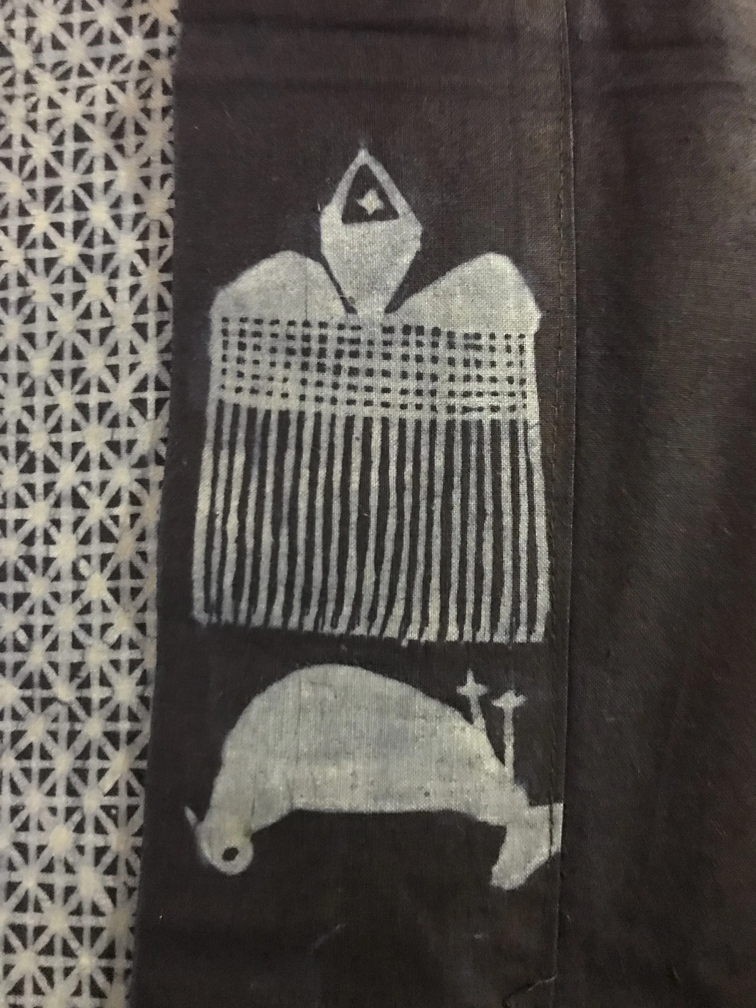 Close-up of black fabric with a white graphic of a dog with a pointed hat, decorated with plus signs and a grid pattern.