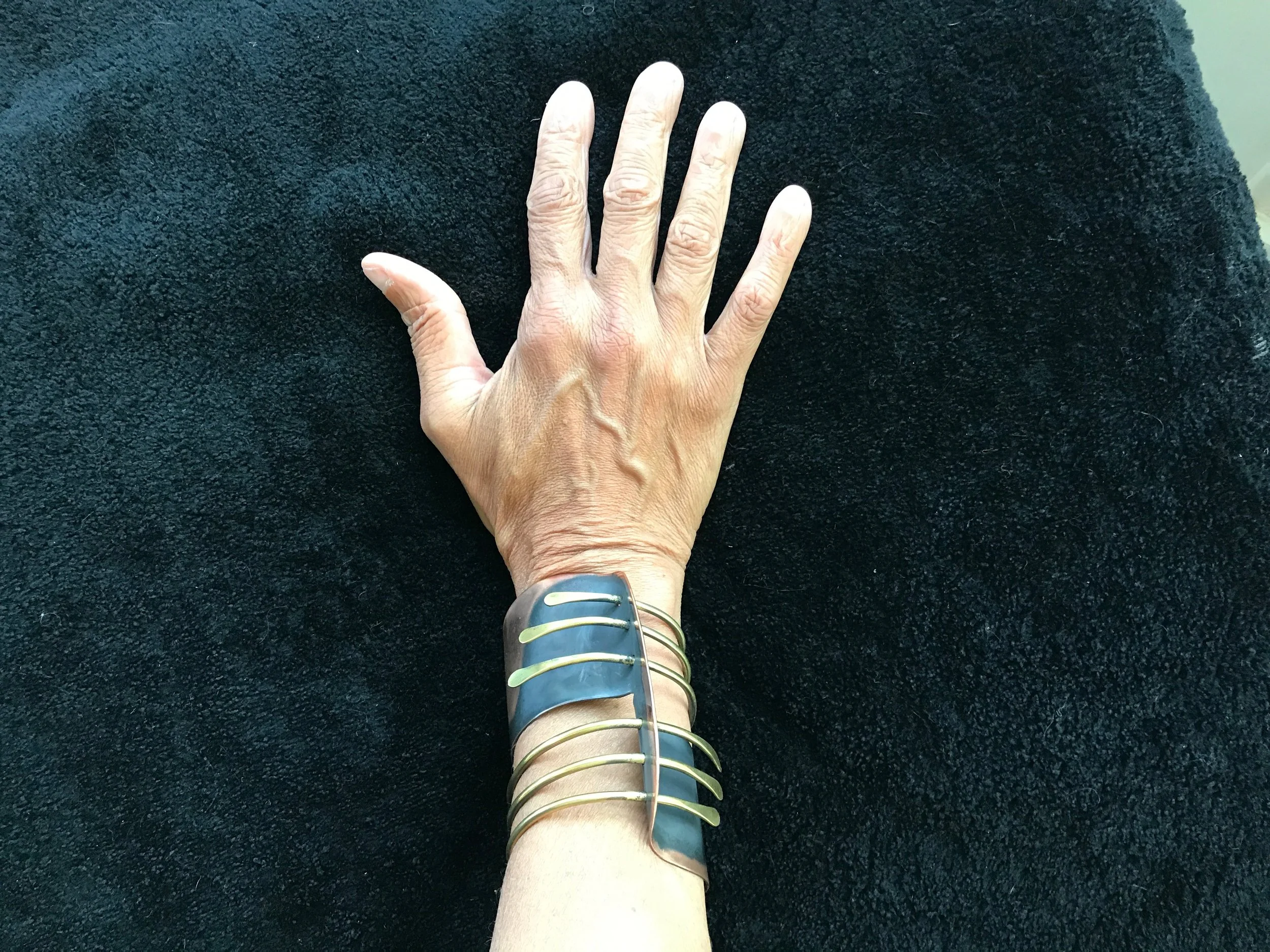A hand resting on a dark textured surface, wearing several metallic and colorful bangles on the wrist.