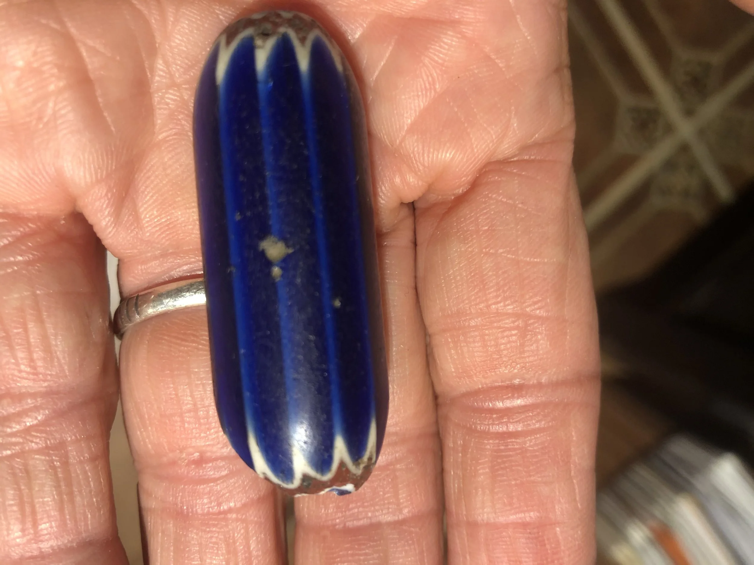 Close-up of a person's finger with painted nail and hand holding a blue, white, and black striped glass marble.