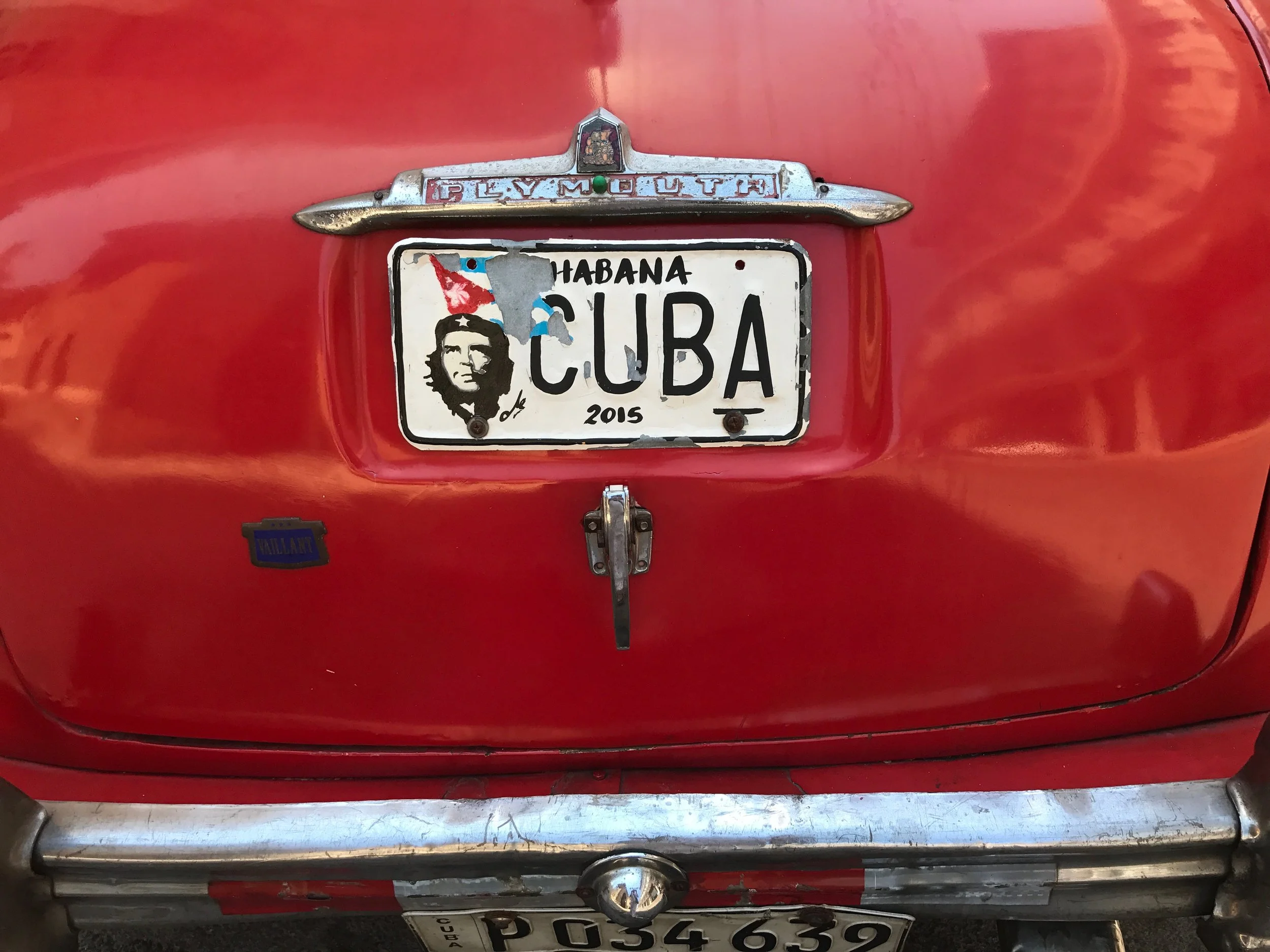 Close-up of a red vintage Plymouth car's rear with a license plate from Cuba and a bumper sticker that says 'Villain'.