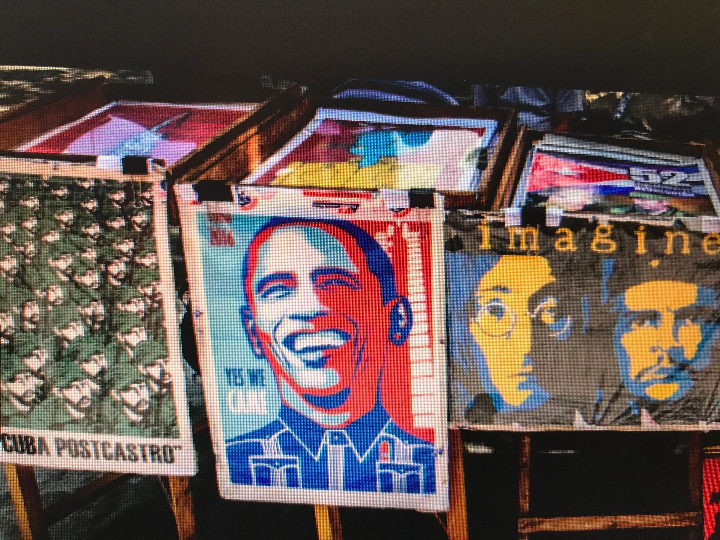 Colorful flags with portraits of Che Guevara and other figures, along with posters and signs at a street market.