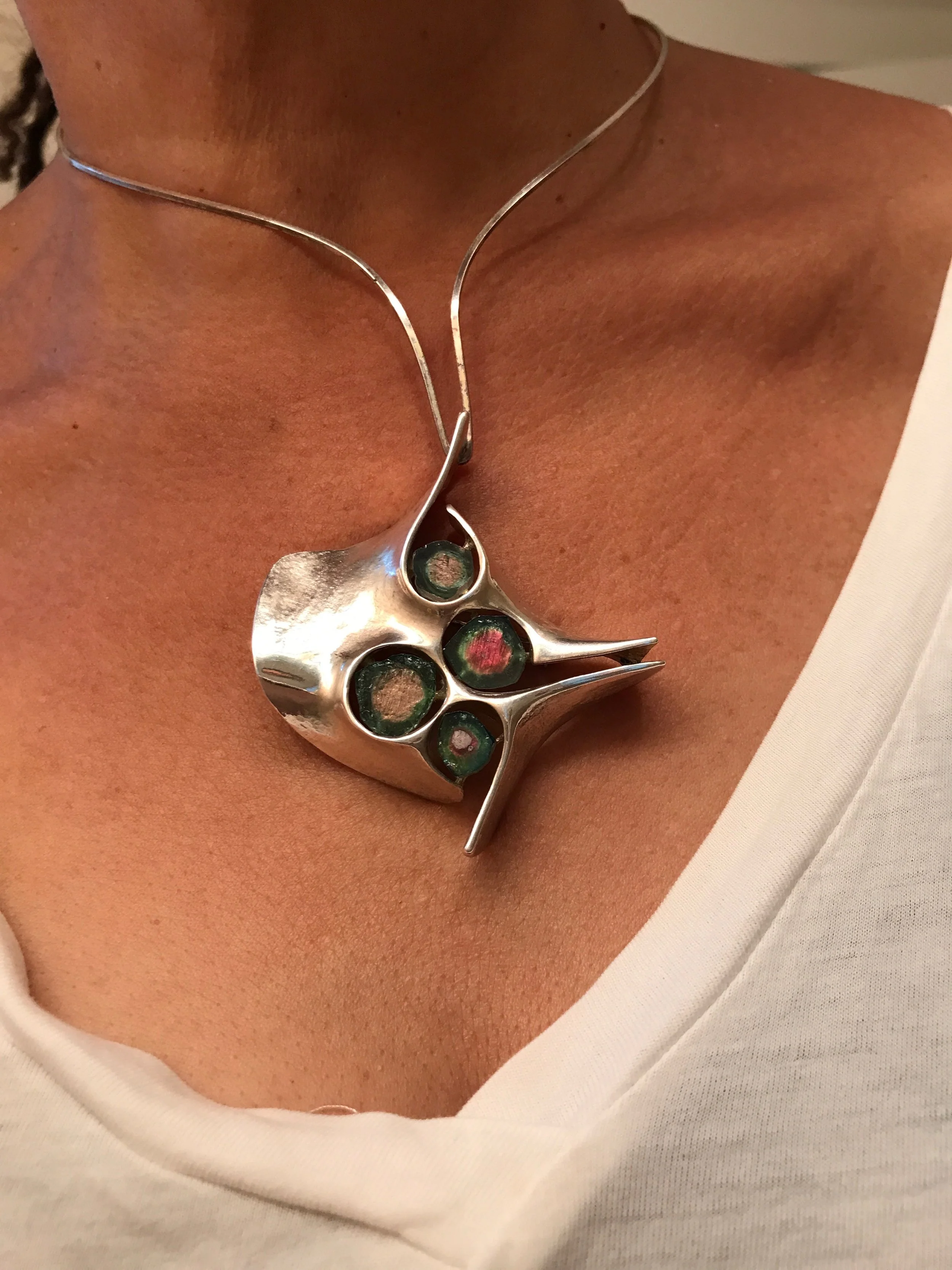 Close-up of a woman's neck and chest wearing a silver necklace with an abstract floral design, layered over a white top.