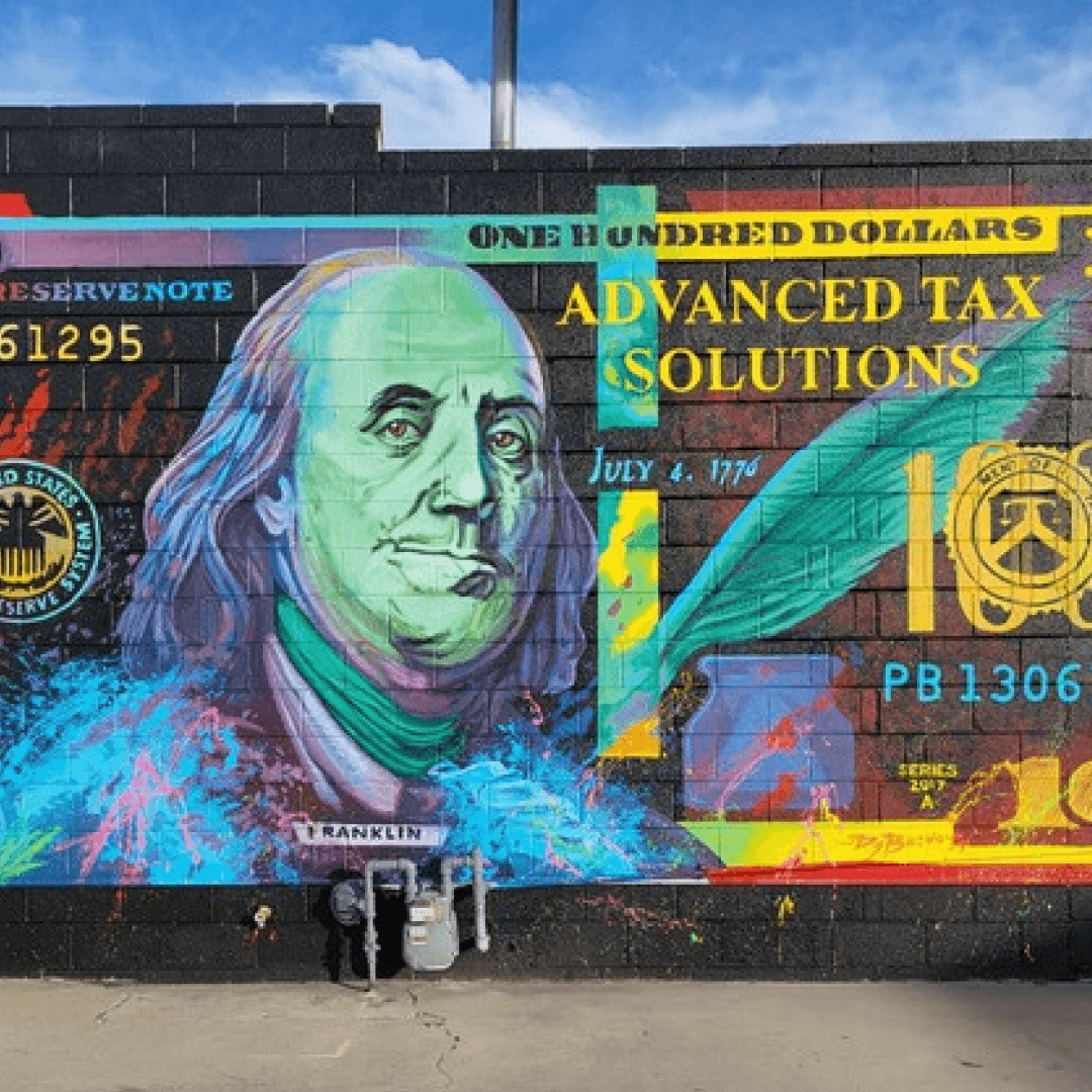 Colorful hand-painted exterior mural reimagining a hundred-dollar bill in bright blues, pinks, and yellows, painted on a business's brick wall.