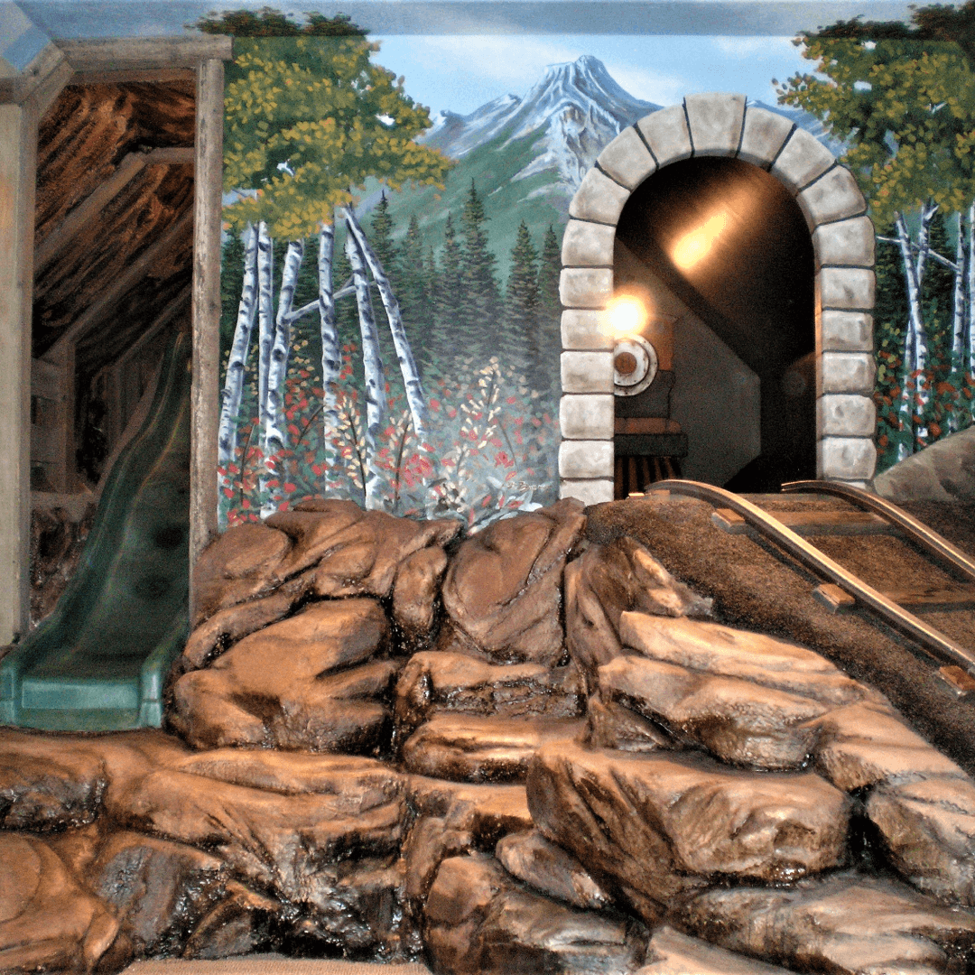 Child's indoor playground with rock climbing, slide, and mountain-themed mural.