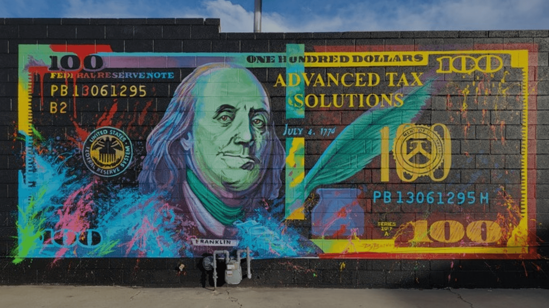 Colorful mural of Benjamin Franklin painted to resemble a hundred-dollar bill, with vibrant splashes of pink, blue, and yellow, featuring text related to taxes and the Federal Reserve.