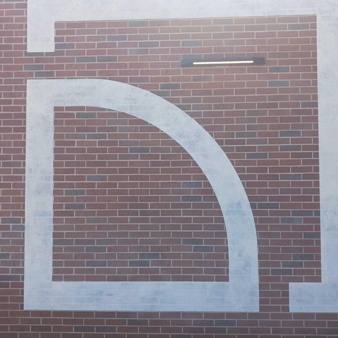 Close-up of a brick wall with a large white painted D-shaped outline and a modern black wall-mounted light fixture above.