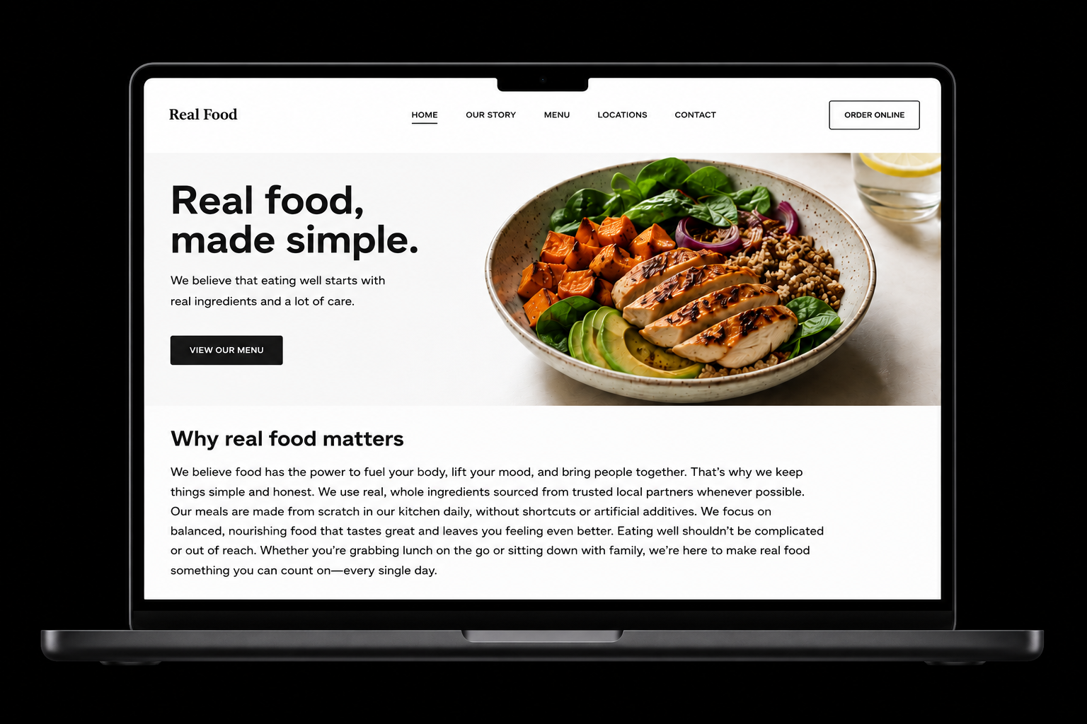 Laptop displaying a webpage for a restaurant called Real Food, featuring a large image of a healthy meal with grilled chicken, sweet potatoes, avocado, spinach, rice, and onion, with a lemon wedge and glass of water in the background.