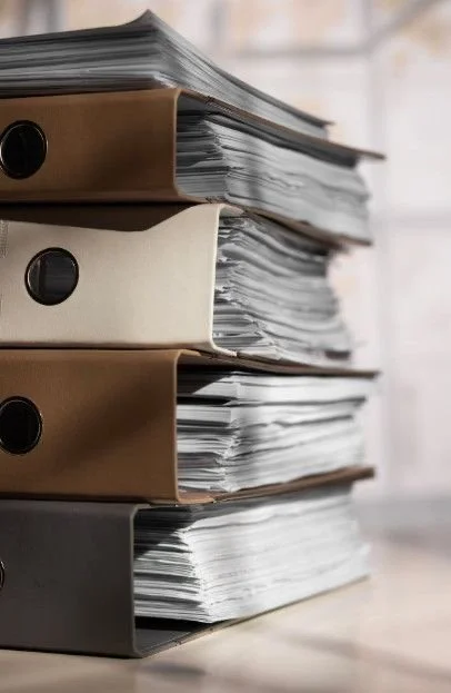 Stack of four ring binders filled with loose papers on a desk.